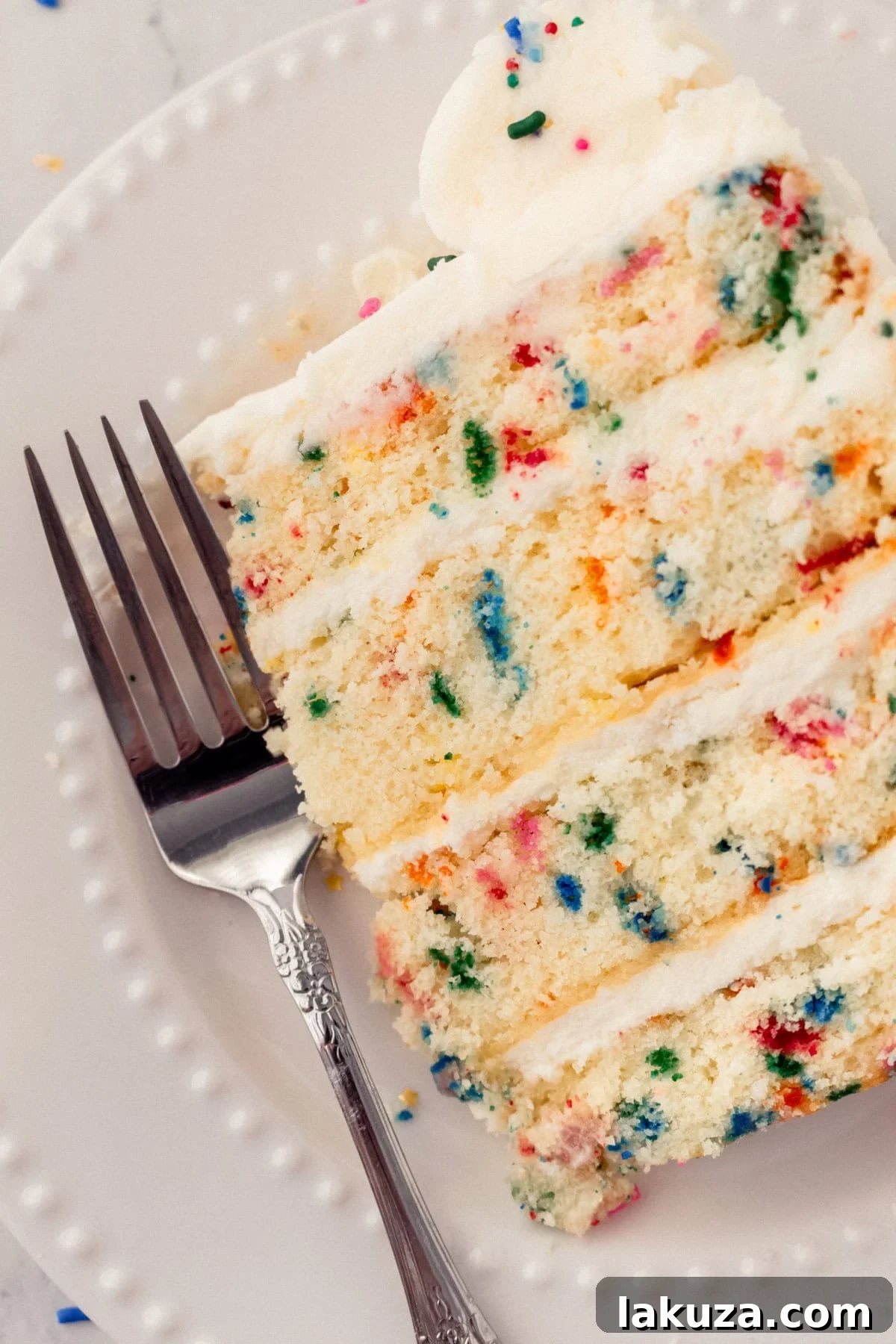 Joyful Sprinkle Celebration 5 A beautifully cut slice of homemade Funfetti cake on a plate, revealing its colorful sprinkle-filled interior and thick layer of cream cheese frosting.