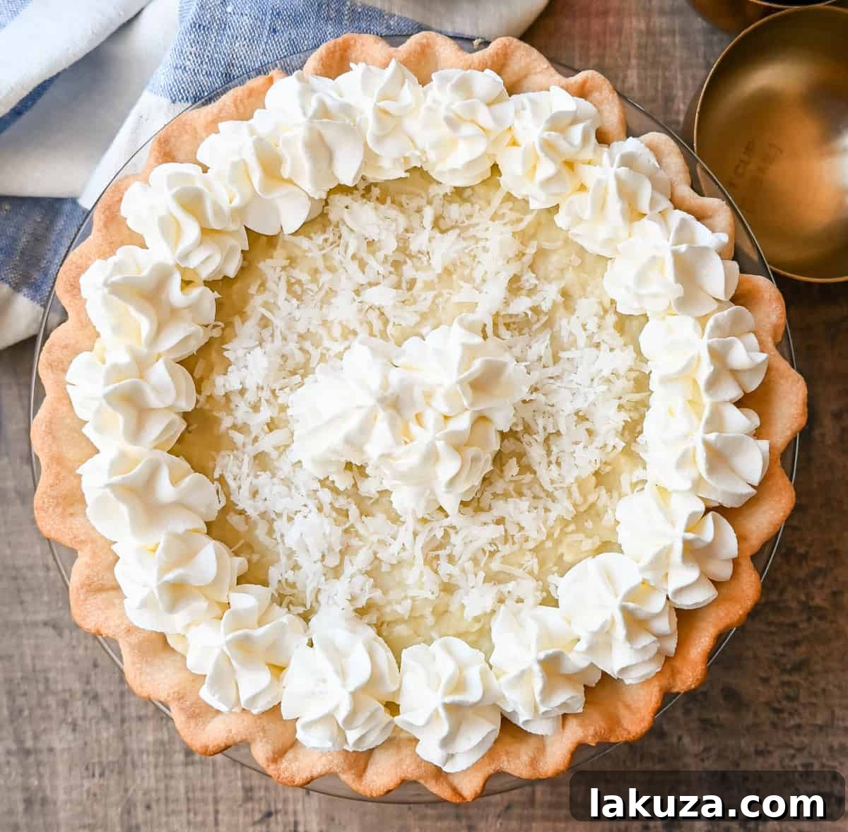 A slice of homemade Coconut Cream Pie with a creamy filling, whipped cream, and toasted coconut on a white plate. This is the famous Dahlia Bakery's secret recipe.
