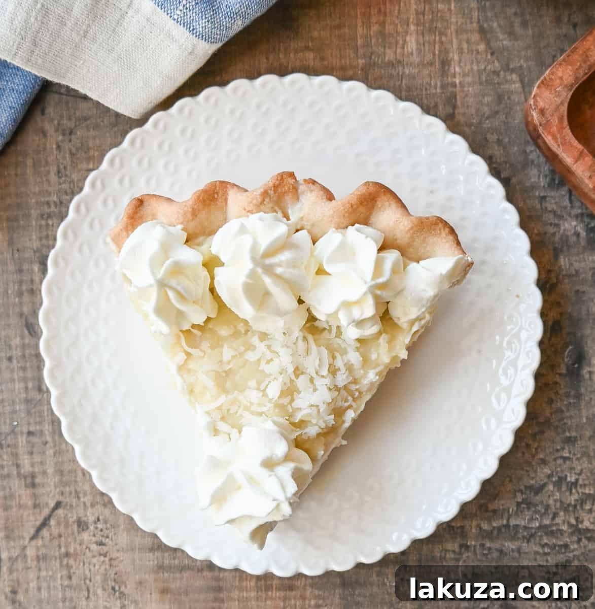 A whole Coconut Cream Pie adorned with fluffy whipped cream and toasted coconut, sitting on a rustic wooden surface.