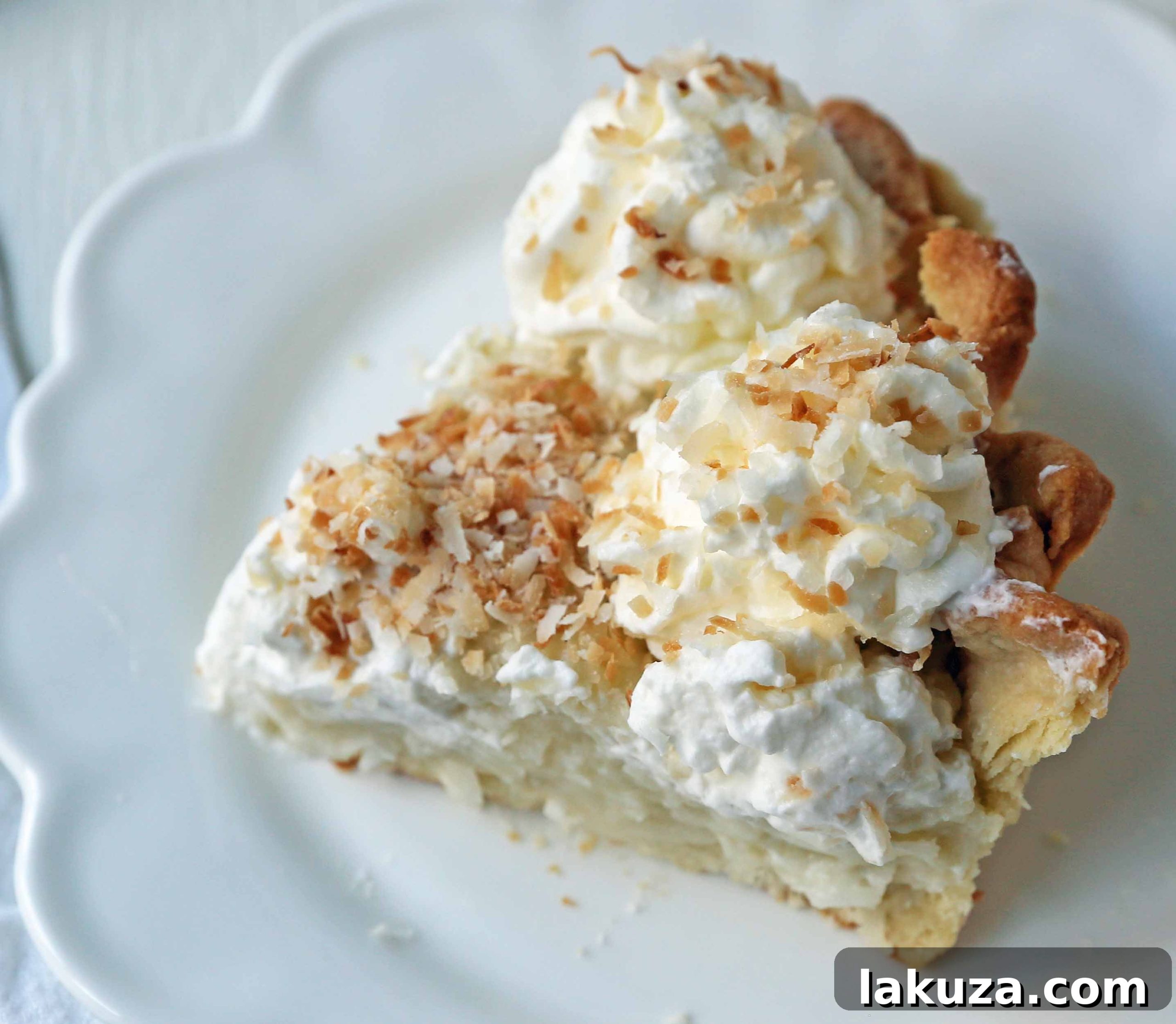A generous slice of Coconut Cream Pie showing layers of crust, custard, and whipped cream, garnished with toasted coconut.