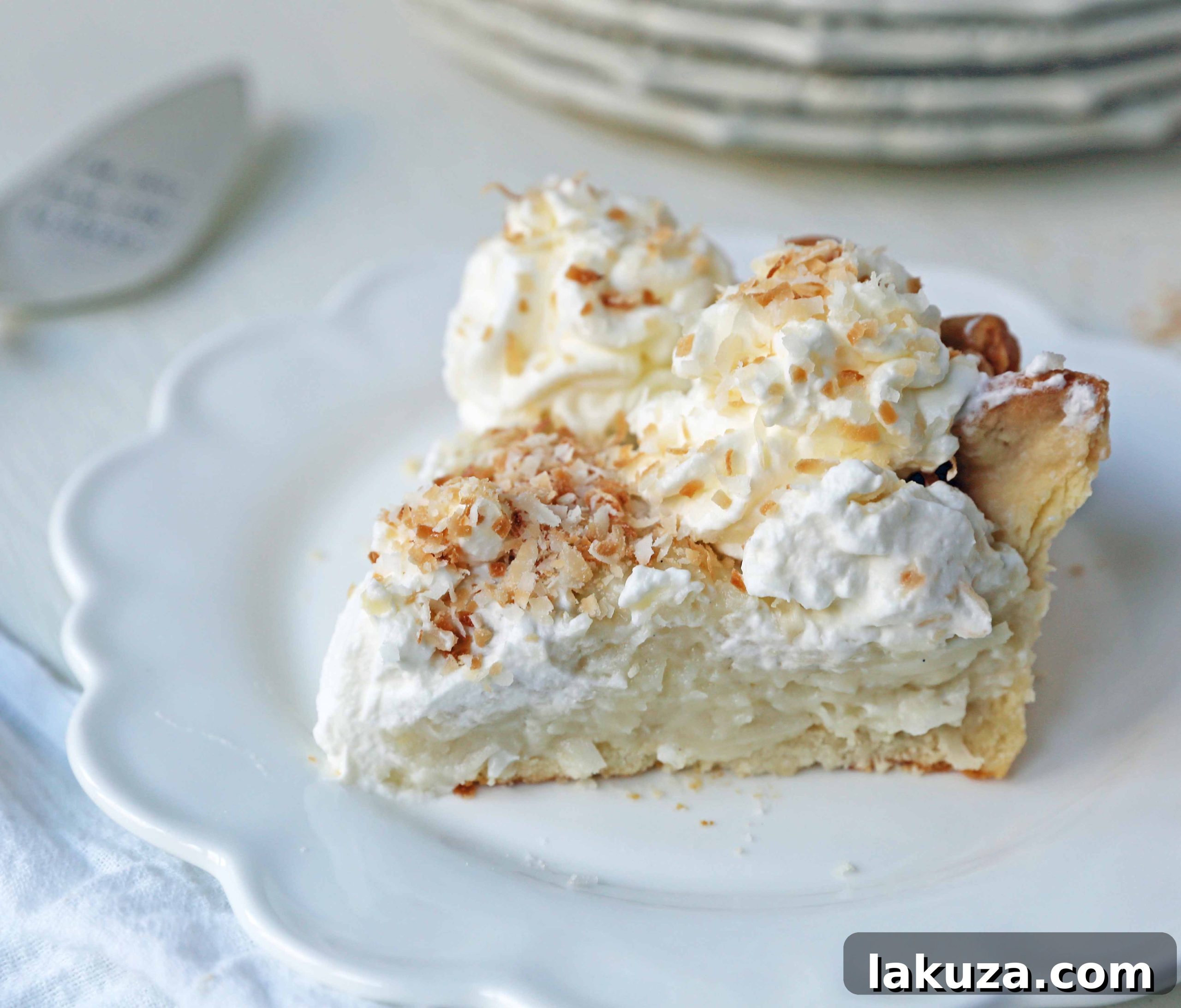 A close-up overhead view of the creamy, white Coconut Cream Pie with swirls of whipped cream and golden toasted coconut flakes.