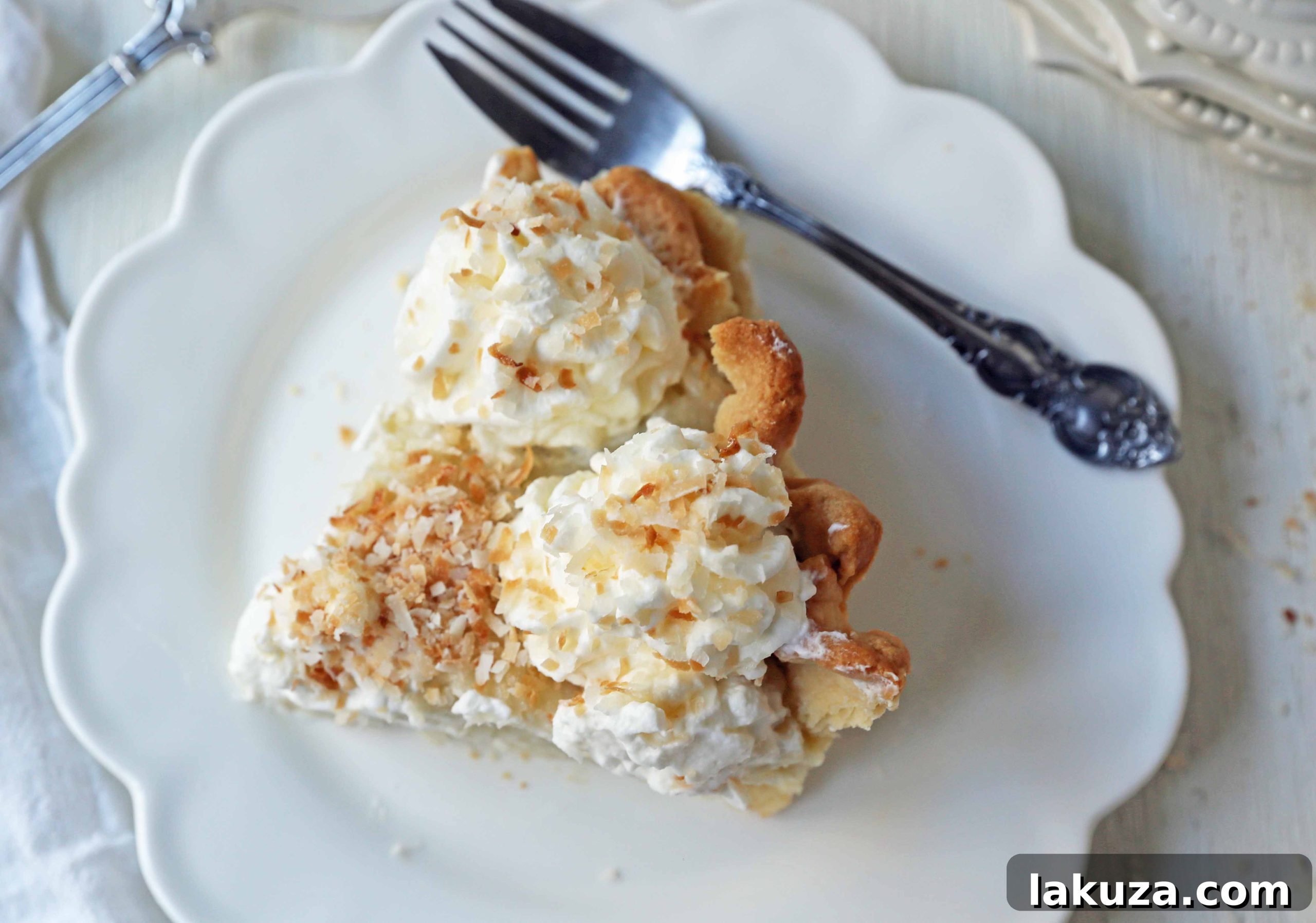 A close-up of a knife cutting a slice of Coconut Cream Pie, revealing its creamy texture and flaky crust.