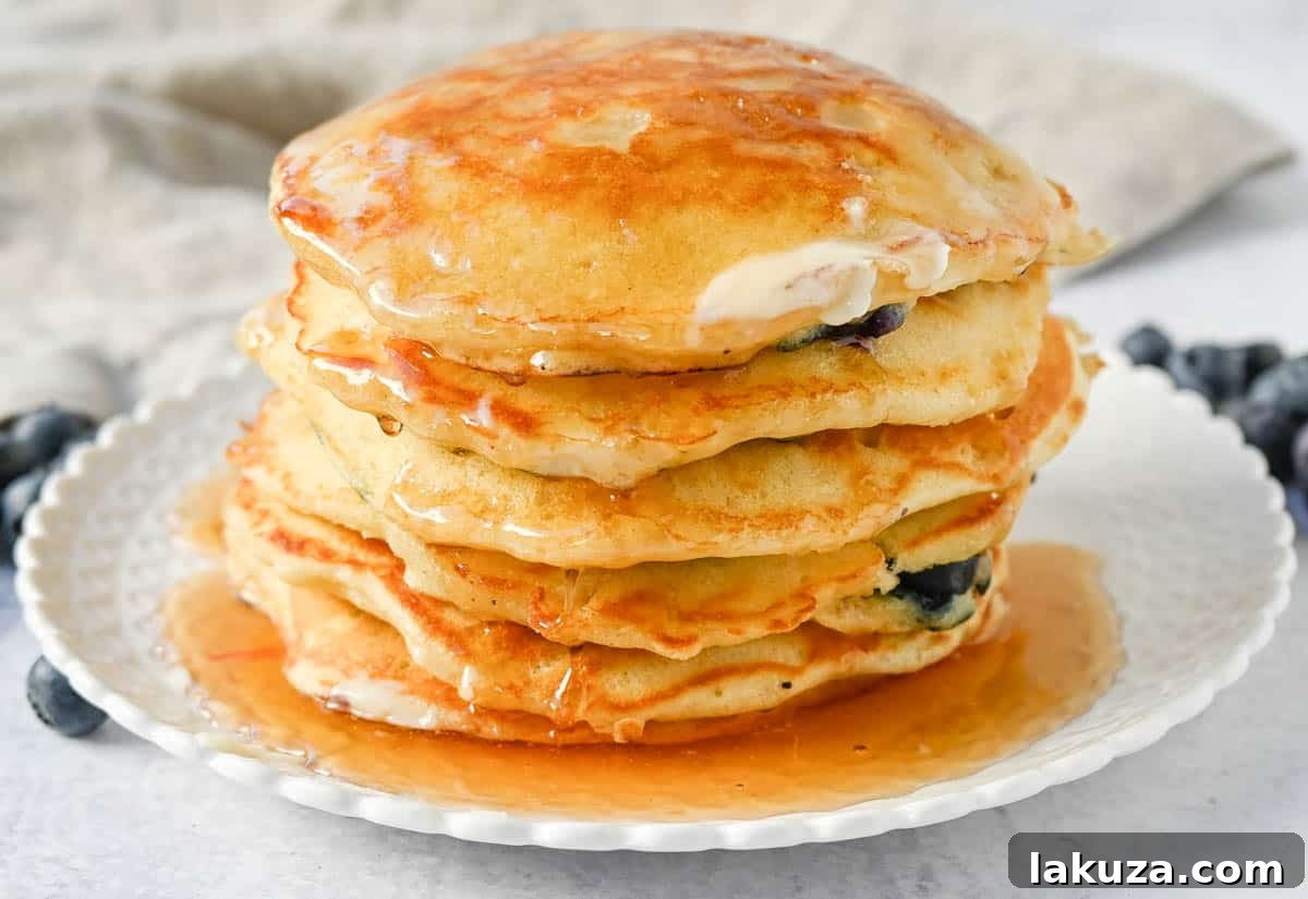 Bursting Blueberry Pancakes 9 Stack of freshly made fluffy blueberry pancakes with butter and syrup, ready to be served.