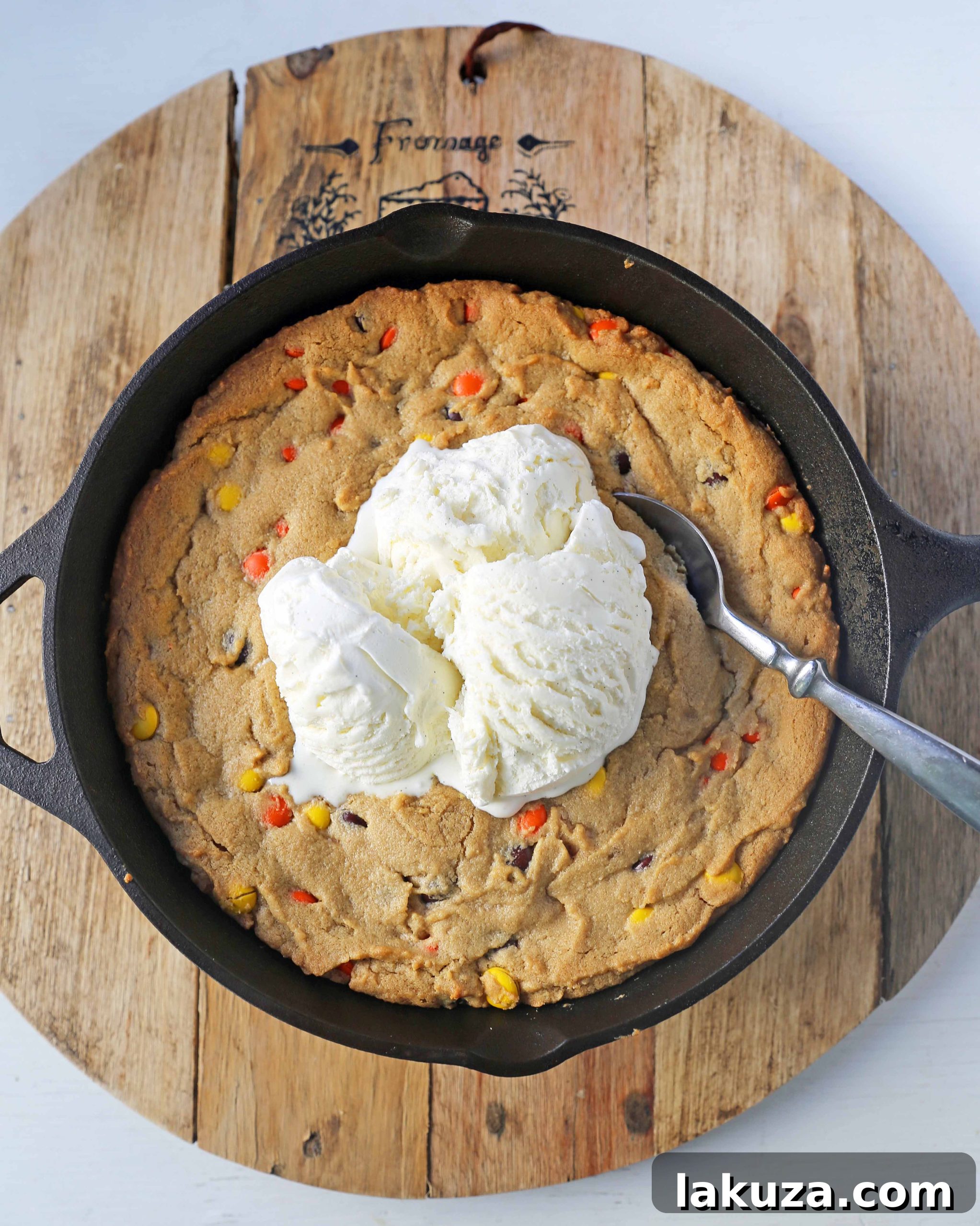 Close-up of a serving of Peanut Butter Skillet Cookie with melted ice cream and hot fudge, showing the gooey texture and Reese's Pieces.