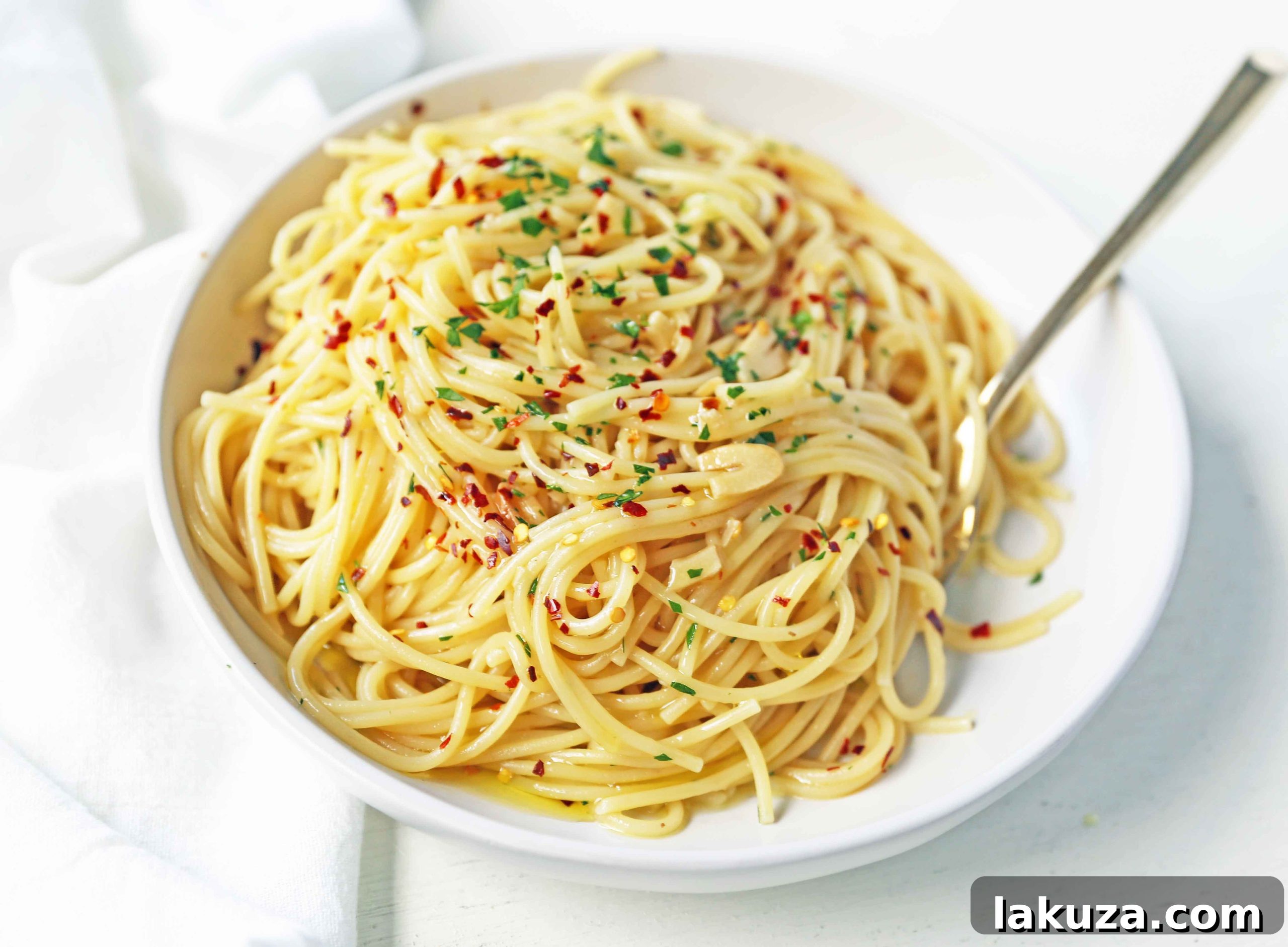 Close-up of freshly prepared Spaghetti Aglio e Olio, showcasing the golden garlic slices, red pepper flakes, and vibrant green parsley.