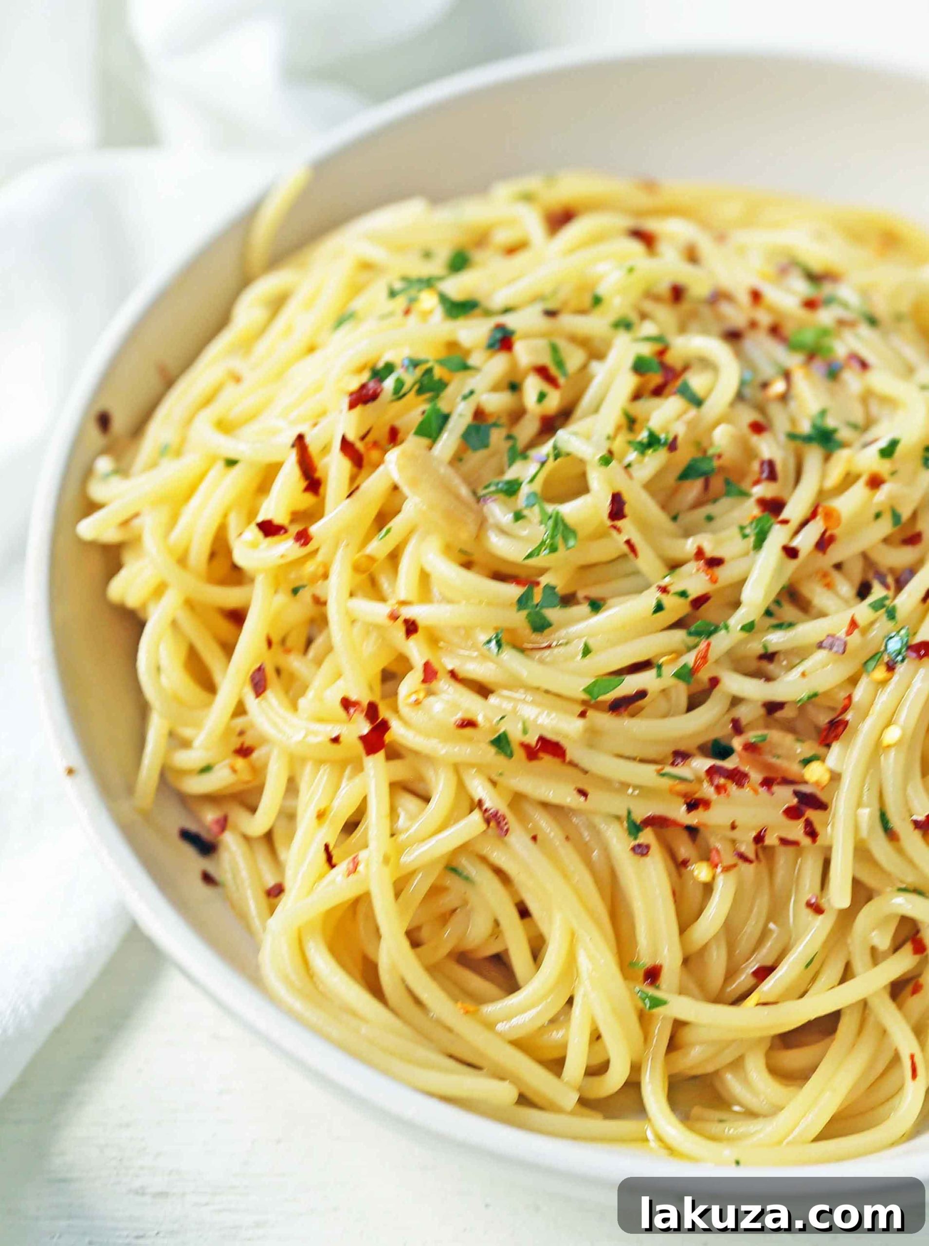 A bowl of Spaghetti Aglio e Olio garnished with fresh parsley and grated Parmesan cheese, ready to be served.