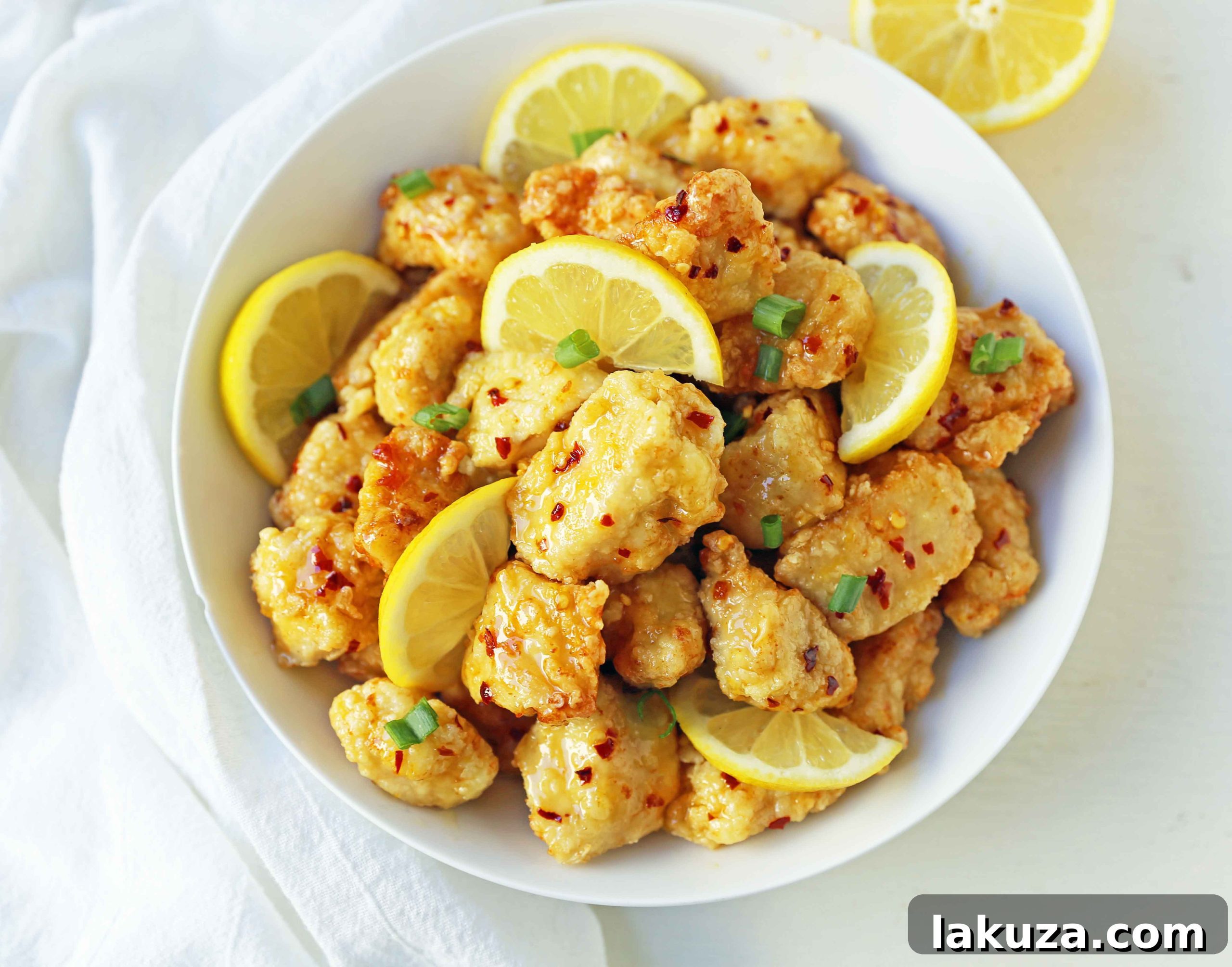 Golden Crispy Lemon Chicken 5 A family-sized serving of homemade Chinese Lemon Chicken, generously coated in a rich lemon sauce and garnished with fresh green onions and lemon zest.