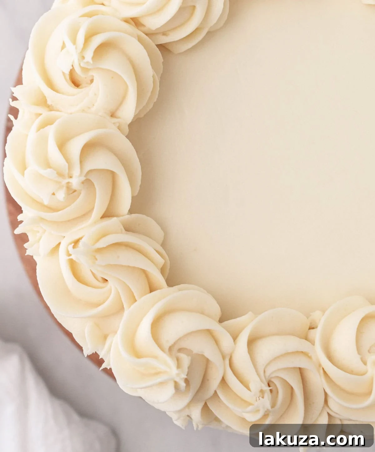 Hands frosting a vanilla layer cake with smooth vanilla buttercream.
