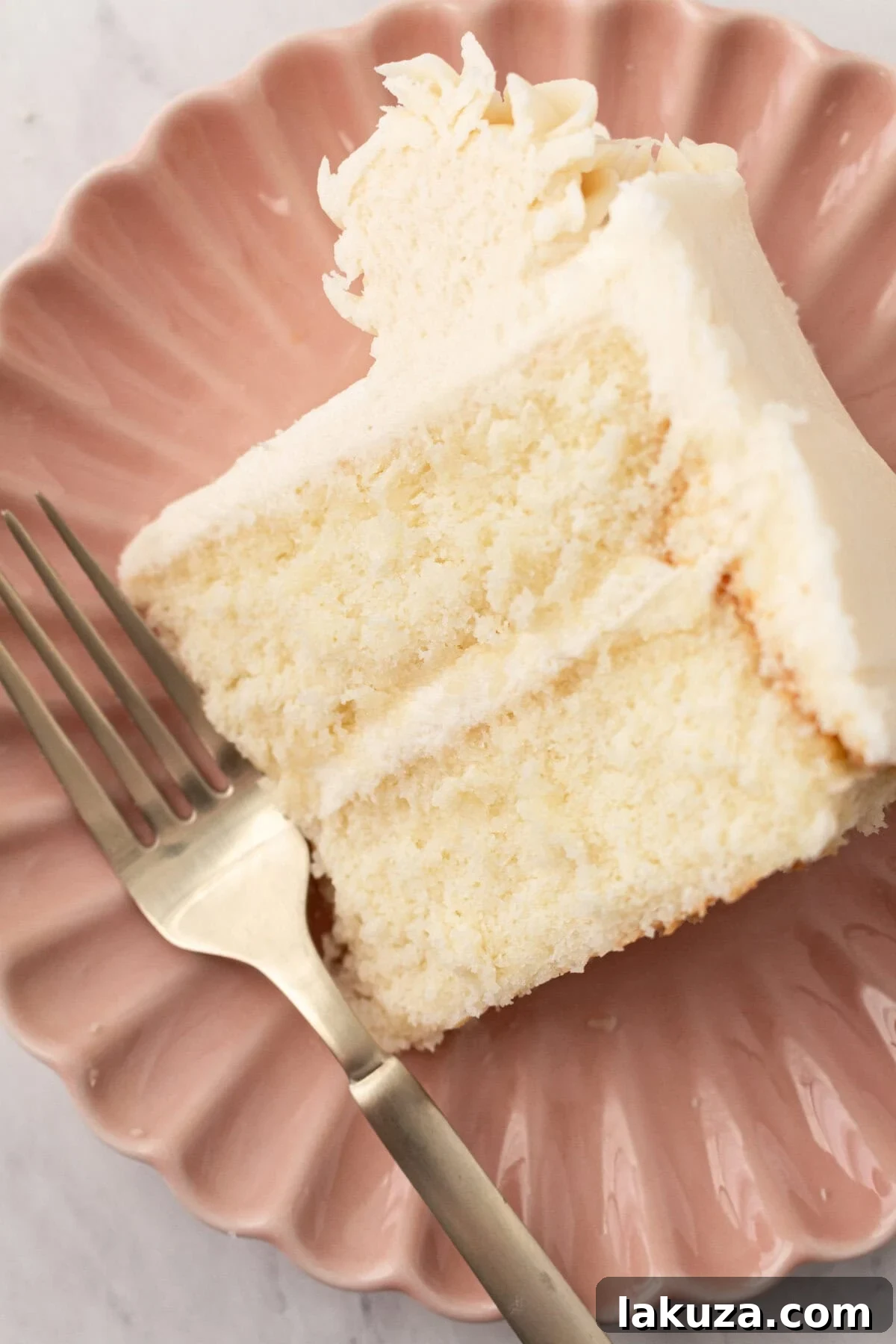 A slice of fluffy vanilla cake on a plate, showcasing its layers and delicious frosting.