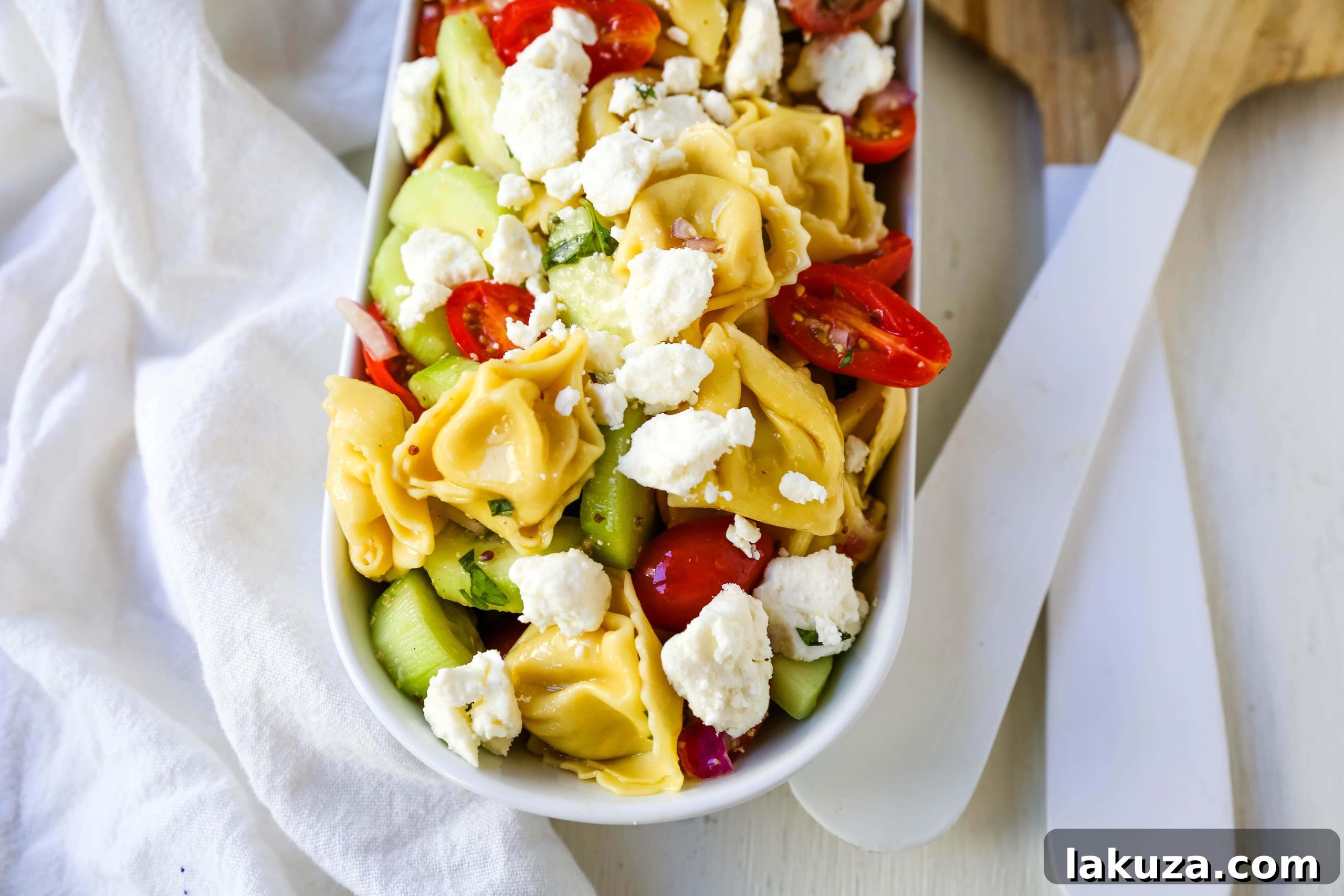 Close-up of Greek Tortellini Pasta Salad showing colorful ingredients: cheese tortellini, halved cherry tomatoes, sliced cucumbers, and feta cheese, coated in a Greek dressing.