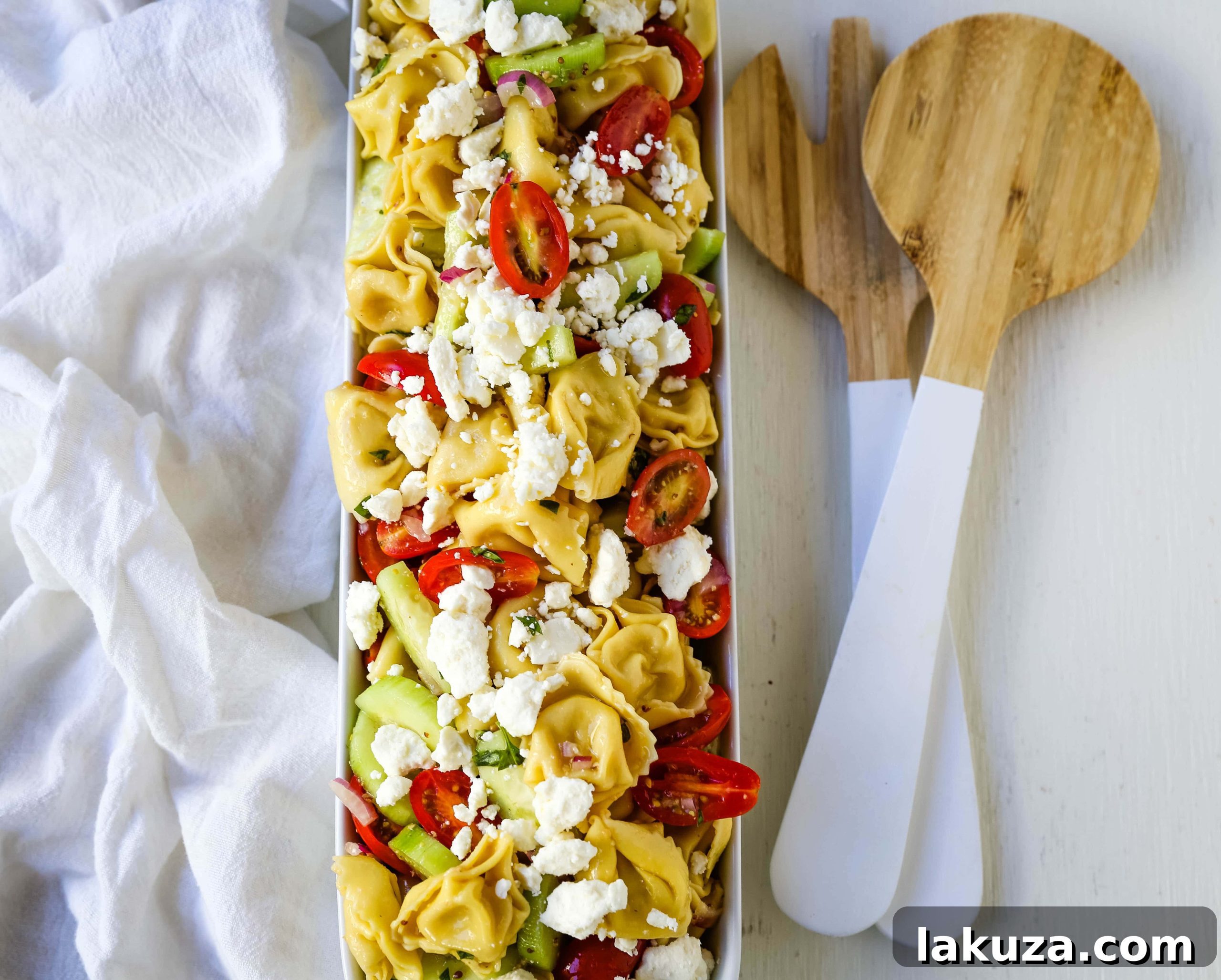 A large bowl of Greek Tortellini Pasta Salad, featuring cheese tortellini, fresh tomatoes, cucumbers, red onion, and crumbled feta, garnished with fresh basil.