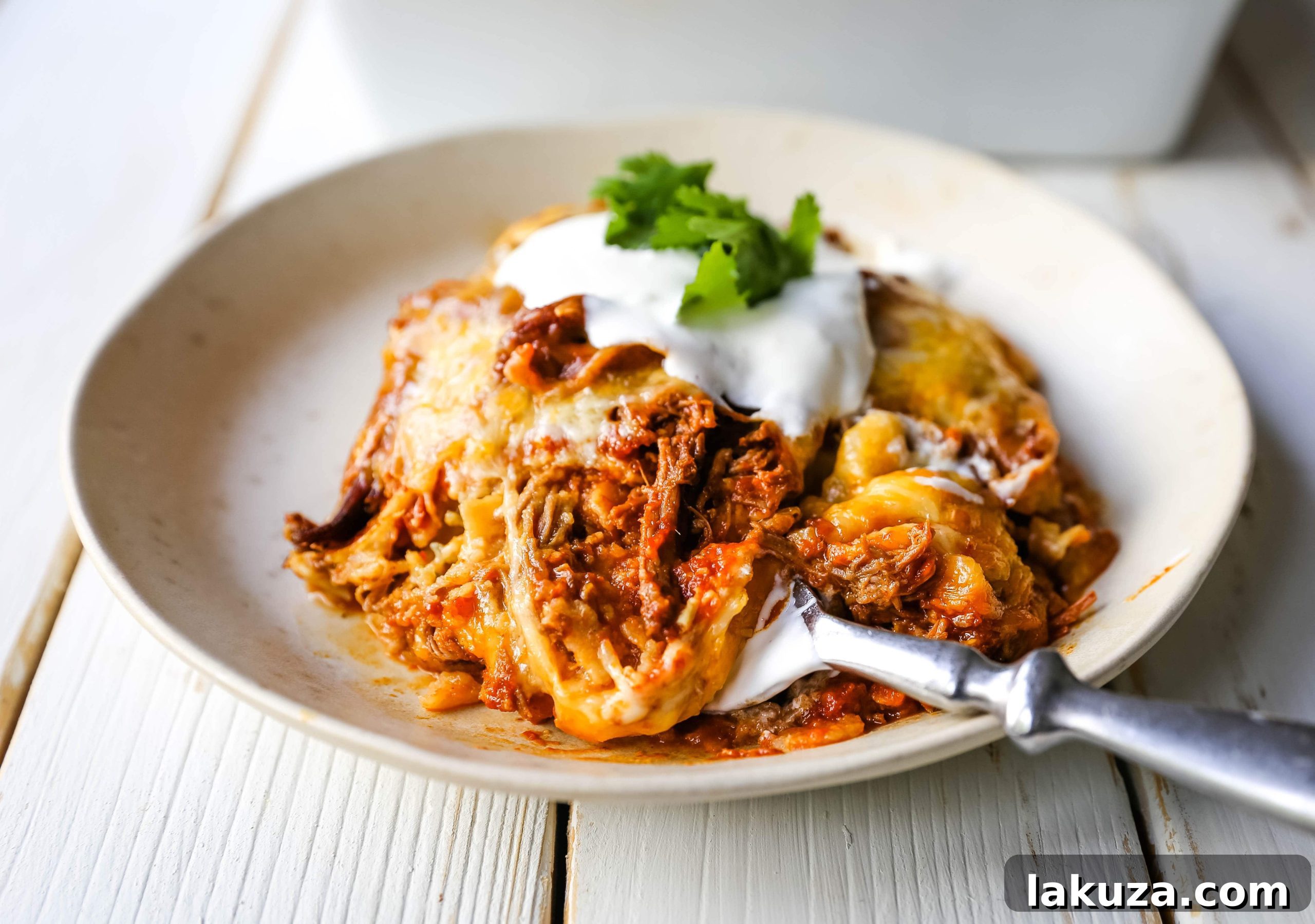 Baked Stacked Beef Enchiladas ready to serve, garnished with sour cream and cilantro. A hearty Mexican casserole with melted cheese and red enchilada sauce.