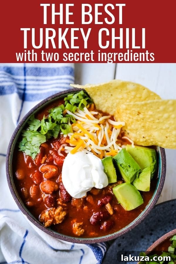 A perfectly plated bowl of turkey chili, topped with cheese, sour cream, and fresh cilantro, on a wooden surface