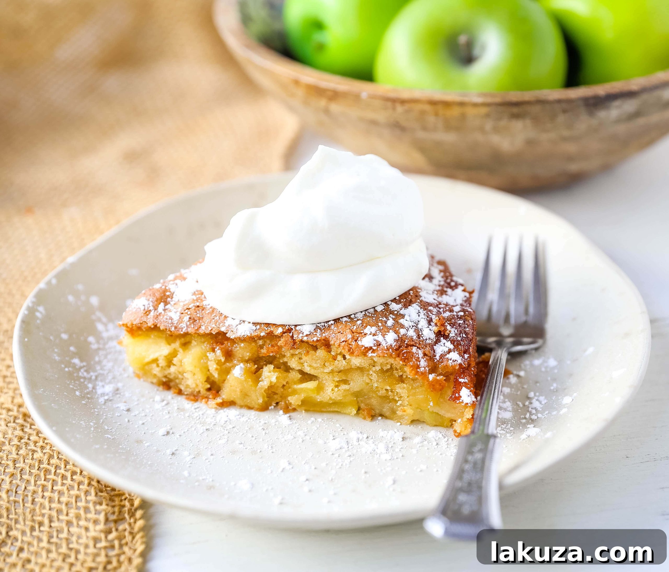 A beautifully rustic French Apple Cake, golden brown and dusted with powdered sugar, ready to be served with freshly whipped cream. An epitome of simple French elegance.
