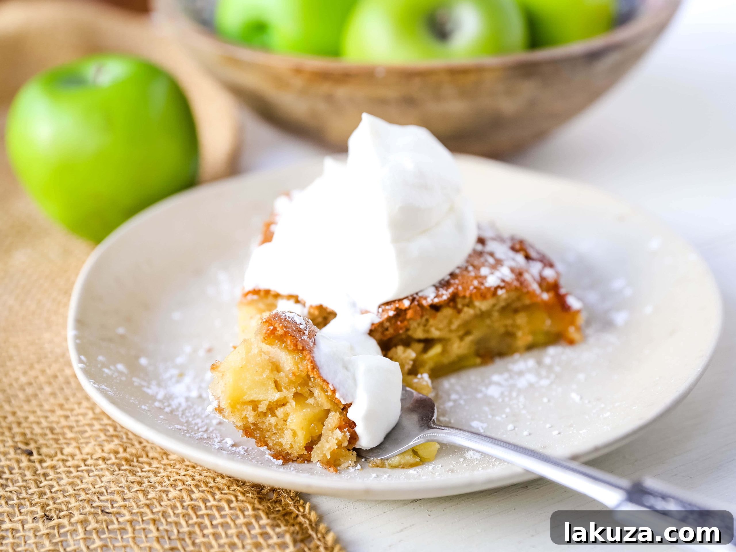 Close-up of a slice of French Apple Cake showcasing the tender cake crumb and perfectly cooked apple pieces, complemented by a swirl of fresh whipped cream. Ideal for a cozy autumn treat.