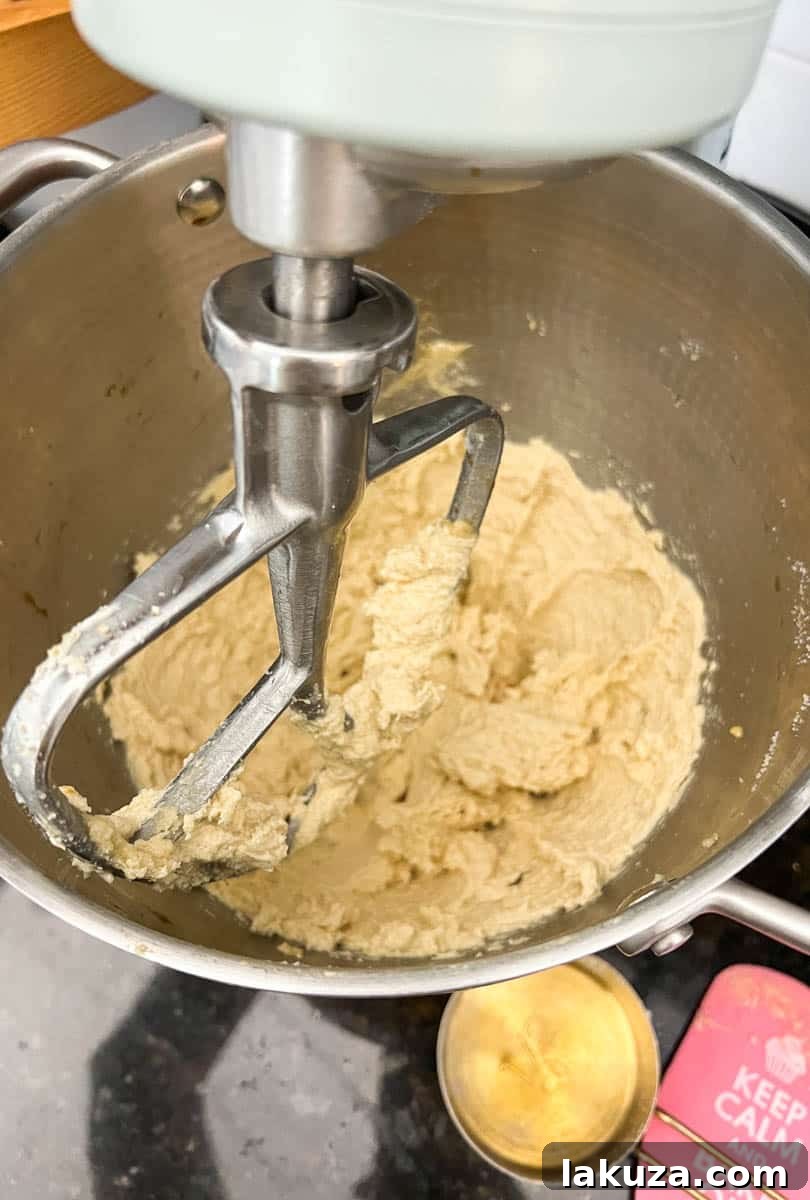 Image showing softened butter, brown sugar, and white sugar being creamed together in a stand mixer bowl, forming a light and fluffy mixture for the double chocolate chip cookie dough.