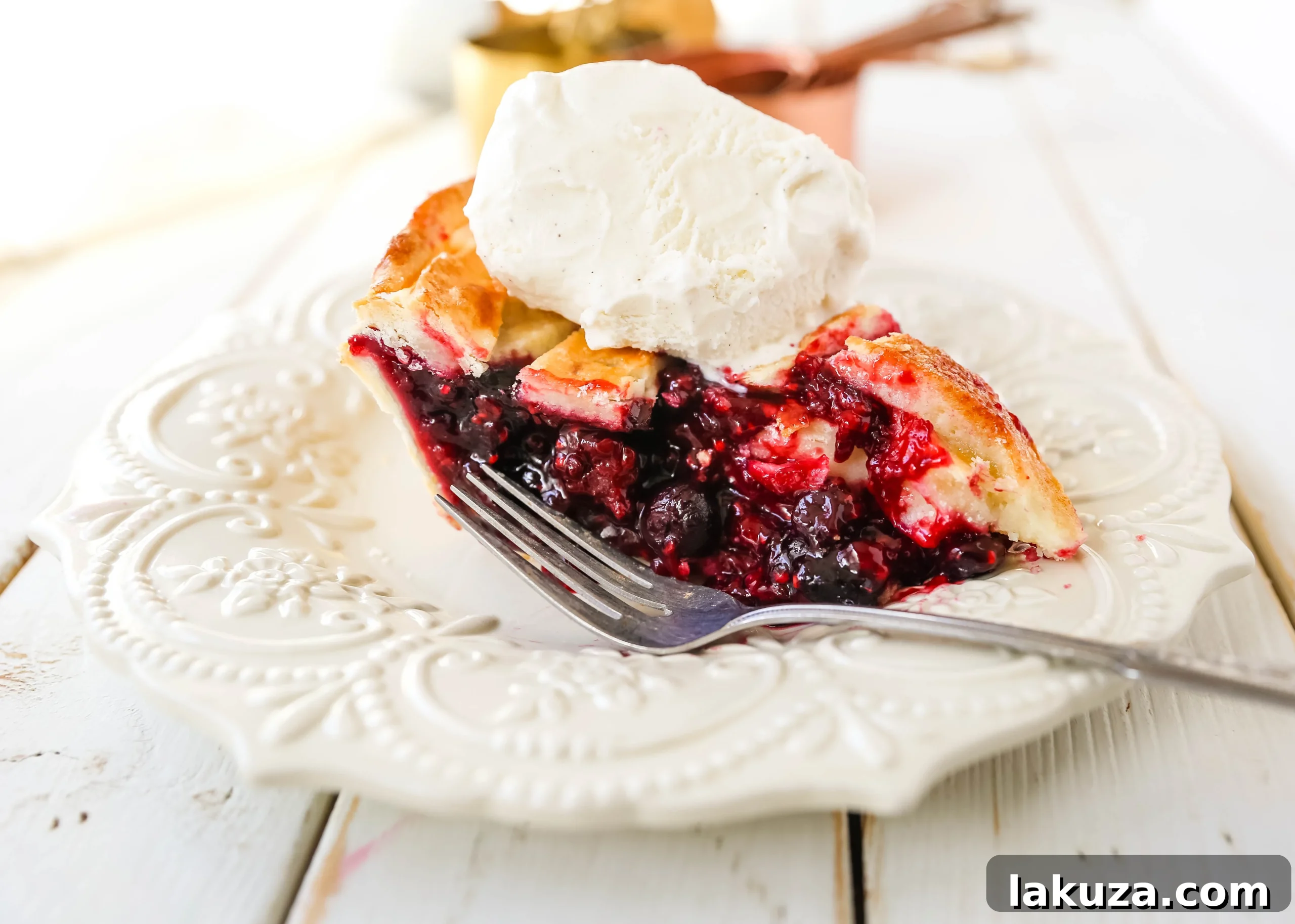 Berry Burst Pie 4 A slice of Triple Berry Pie on a white plate, revealing layers of juicy berries and a perfectly baked, flaky crust. Ready to be enjoyed with a dollop of ice cream.