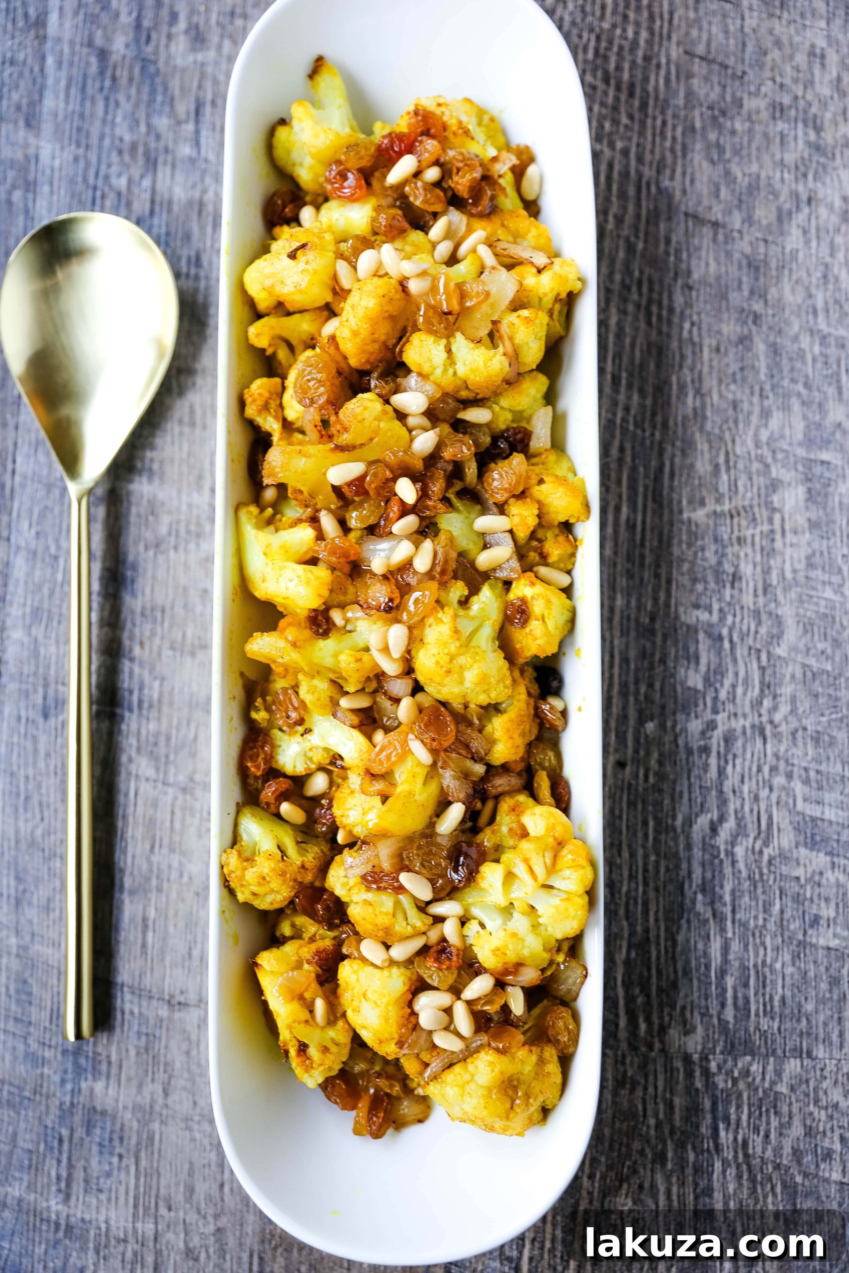 Close-up of vibrant Turmeric Roasted Cauliflower with caramelized onions, golden raisins, and pine nuts, ready to serve.