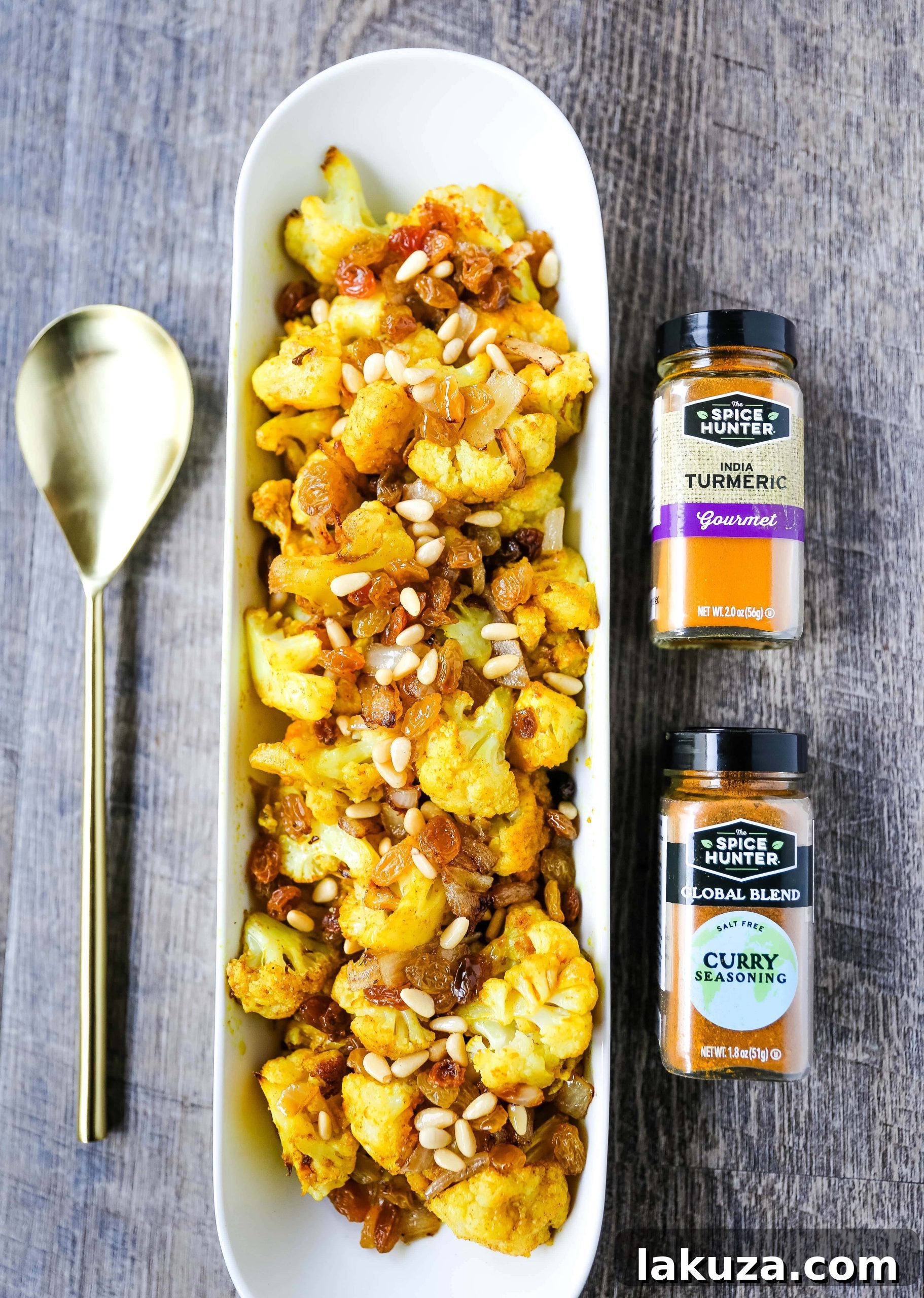 Indian Spiced Roasted Cauliflower with colorful spices, golden raisins, and pine nuts on a baking sheet.