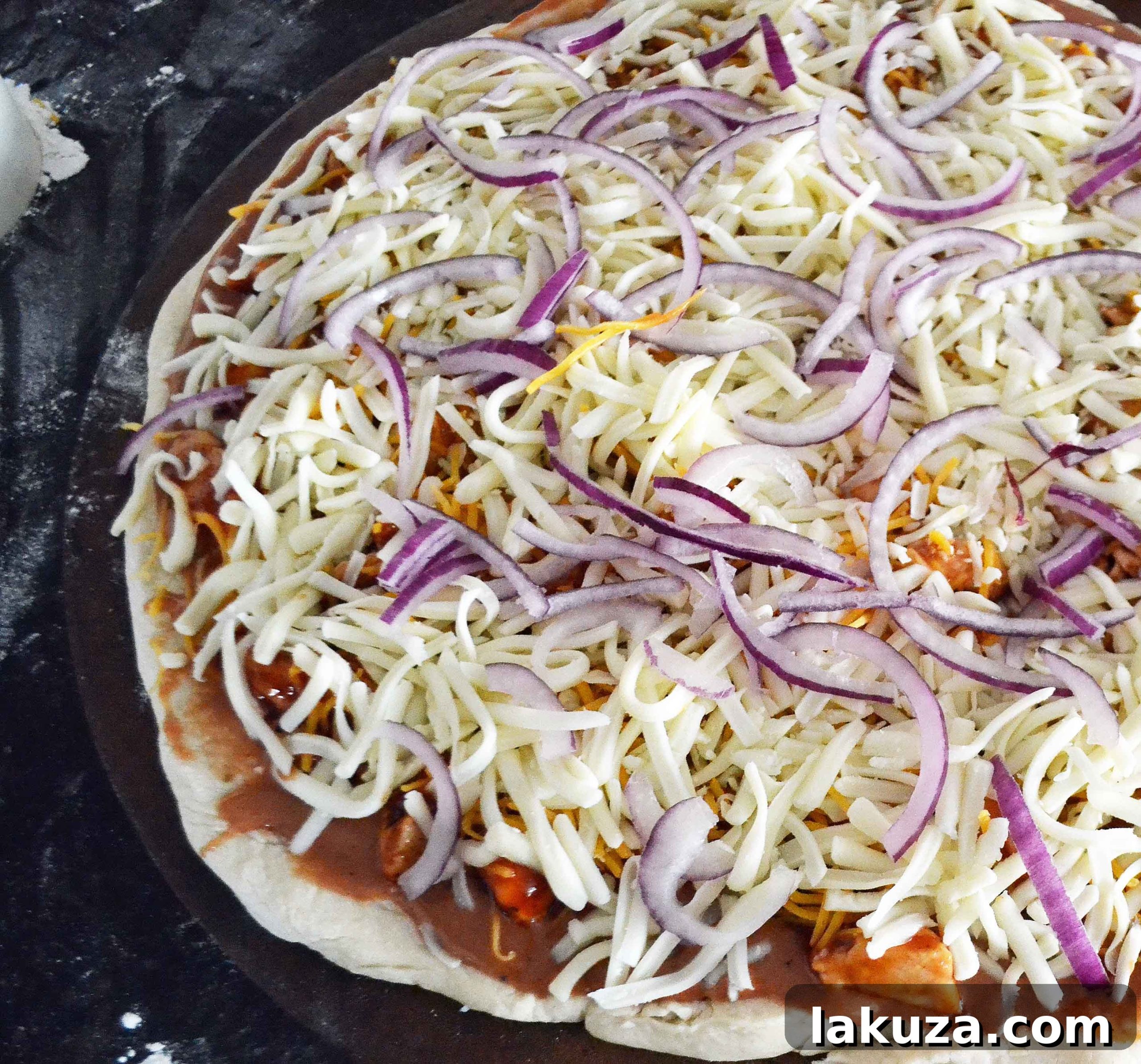 Gourmet BBQ Chicken Pizza at Home 8 Freshly assembled BBQ Chicken Pizza, topped with cheese, chicken, and red onion, prior to baking.