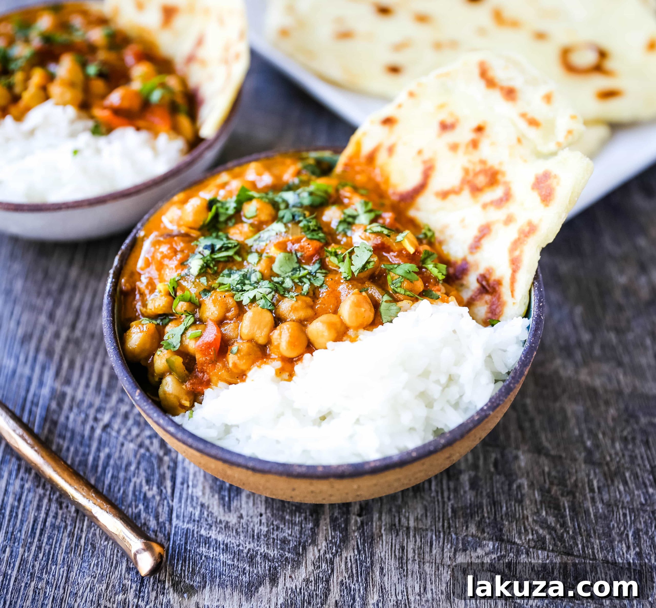 A beautifully plated bowl of vegan Coconut Chickpea Curry, garnished with fresh cilantro and served with a side of naan bread.