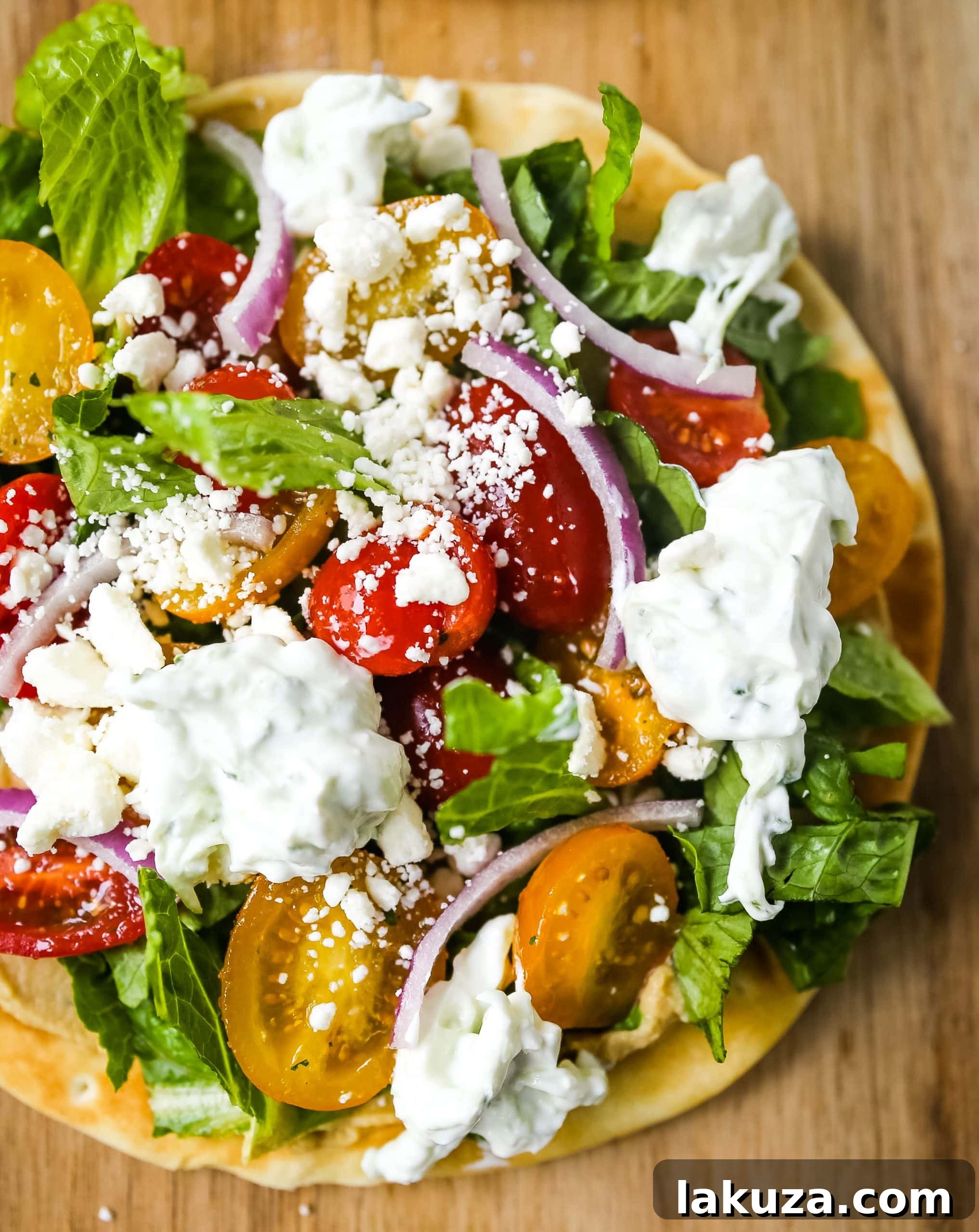 Zesty Greek Pita Pizzas 6 A close-up of a completed Greek Salad Pita Pizza, garnished with fresh dill, showing the vibrant mix of ingredients including feta cheese, red onion, and plenty of creamy tzatziki, ready to be served.