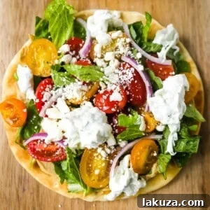 Zesty Greek Pita Pizzas 8 A close-up image of a Greek Salad Pita Pizza, topped with fresh vegetables and tzatziki.