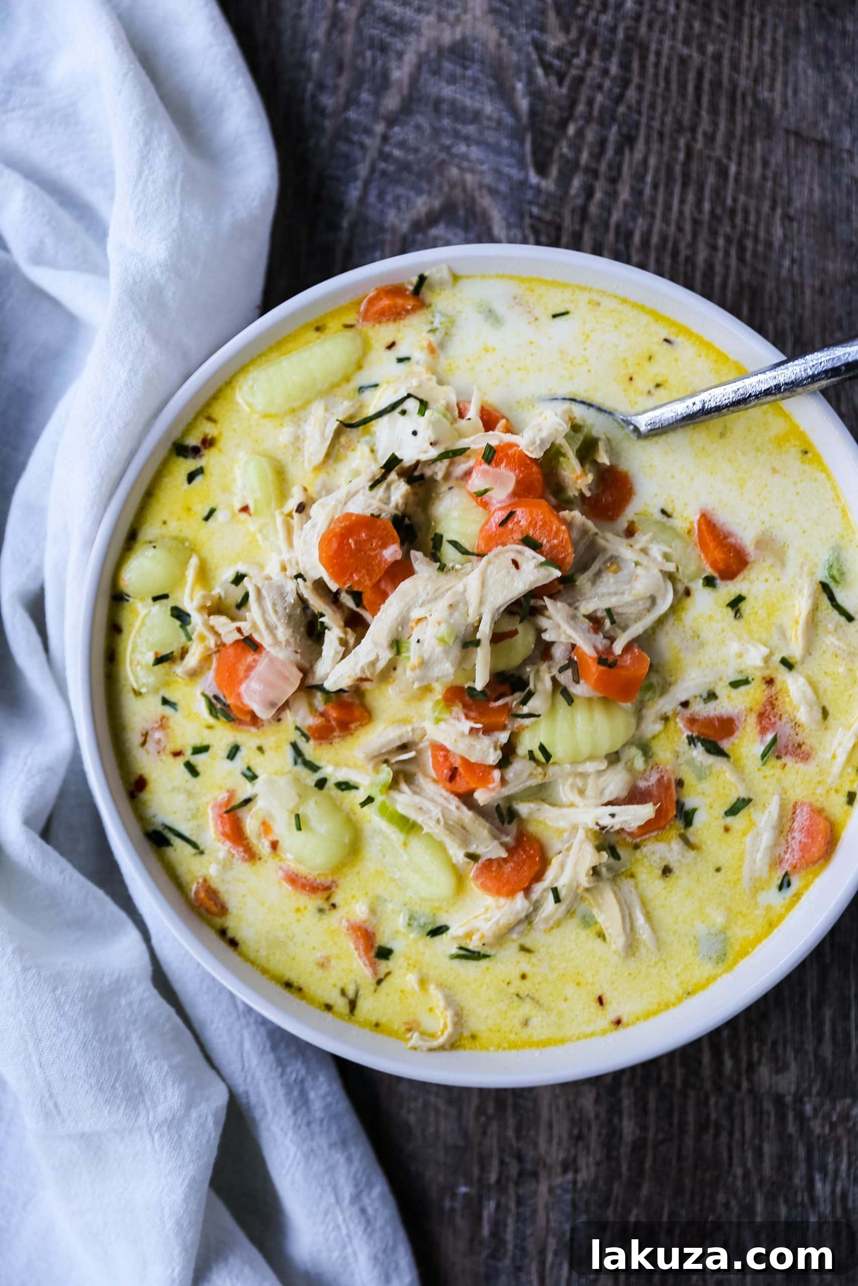 Bowl of creamy gnocchi chicken soup with fresh herbs and a spoon, ready to eat.