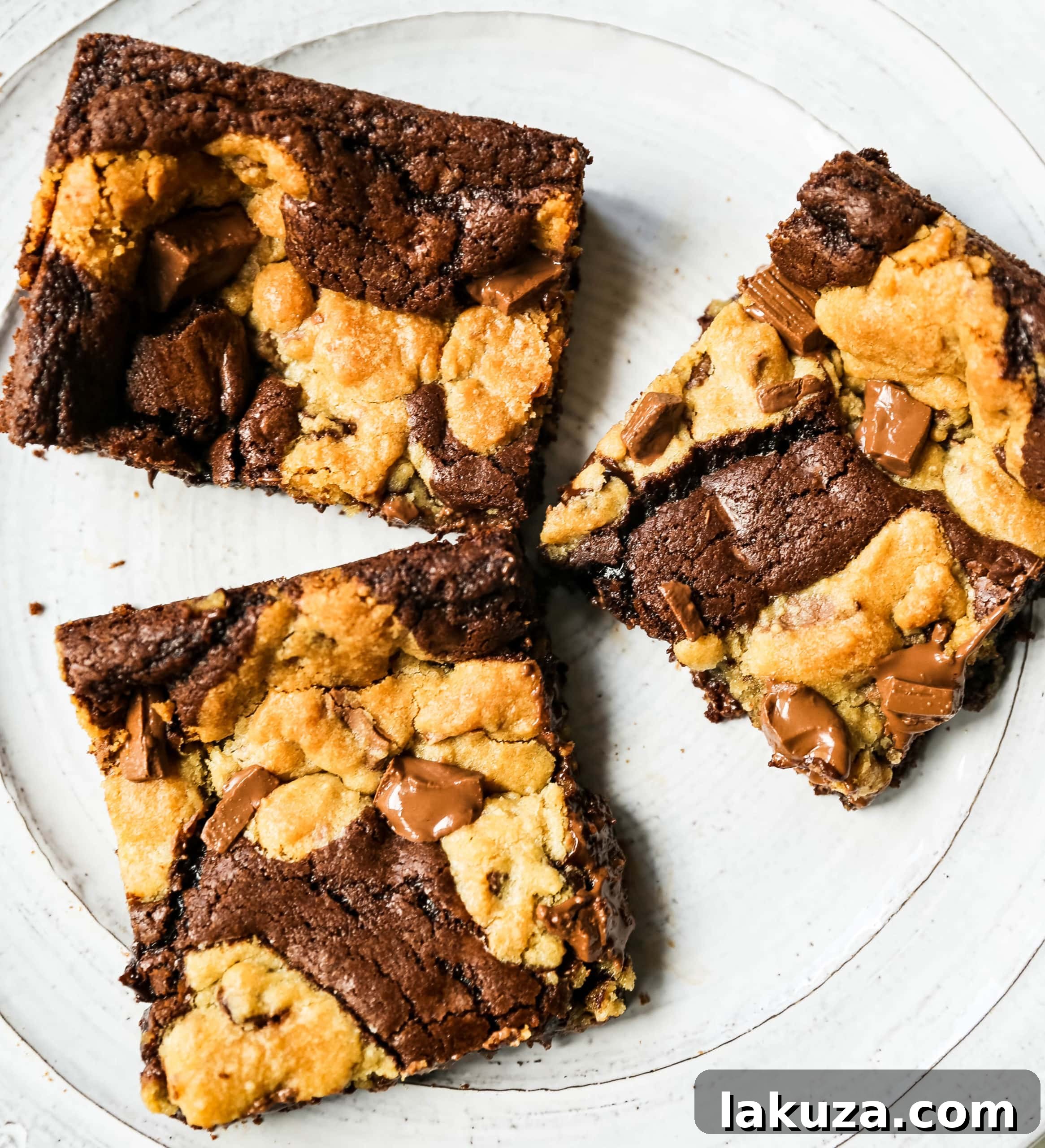 Hand holding a fresh, warm brookie bar, showcasing the thick brownie base and the golden-brown chocolate chip cookie topping.