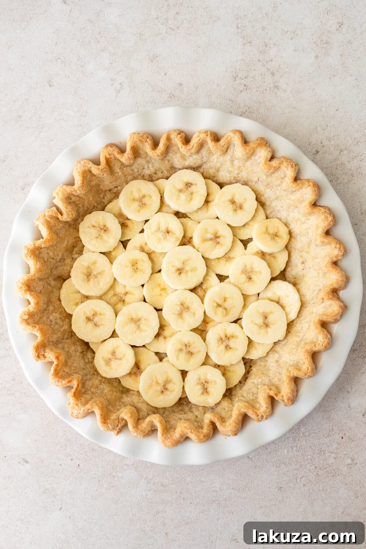 Sliced bananas neatly arranged in a pre-baked pie crust, forming the foundational layer of the easy banana cream pie.