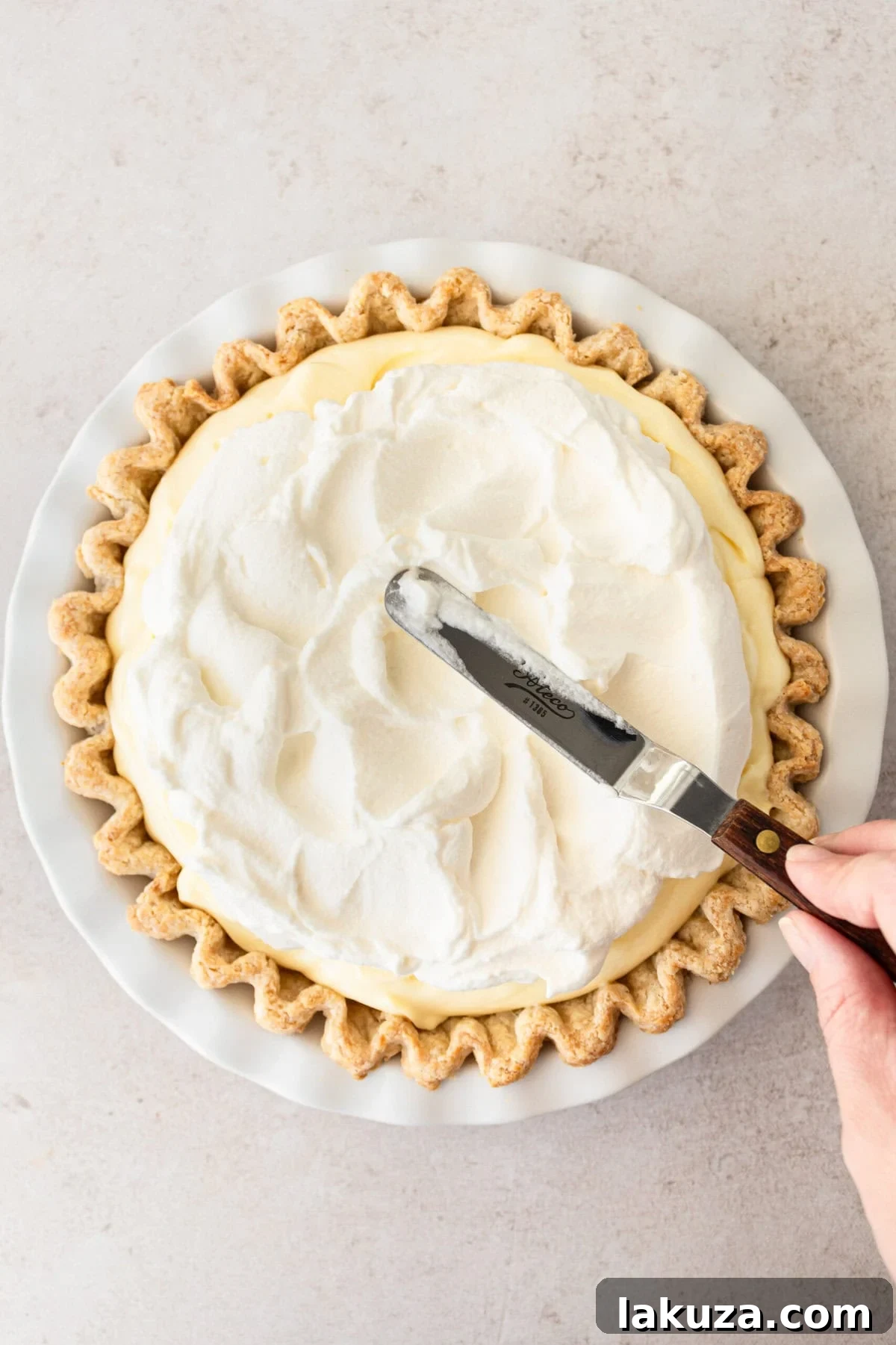 Spreading a thick, even layer of freshly whipped cream, sweetened with powdered sugar, over the top of the banana cream pie.
