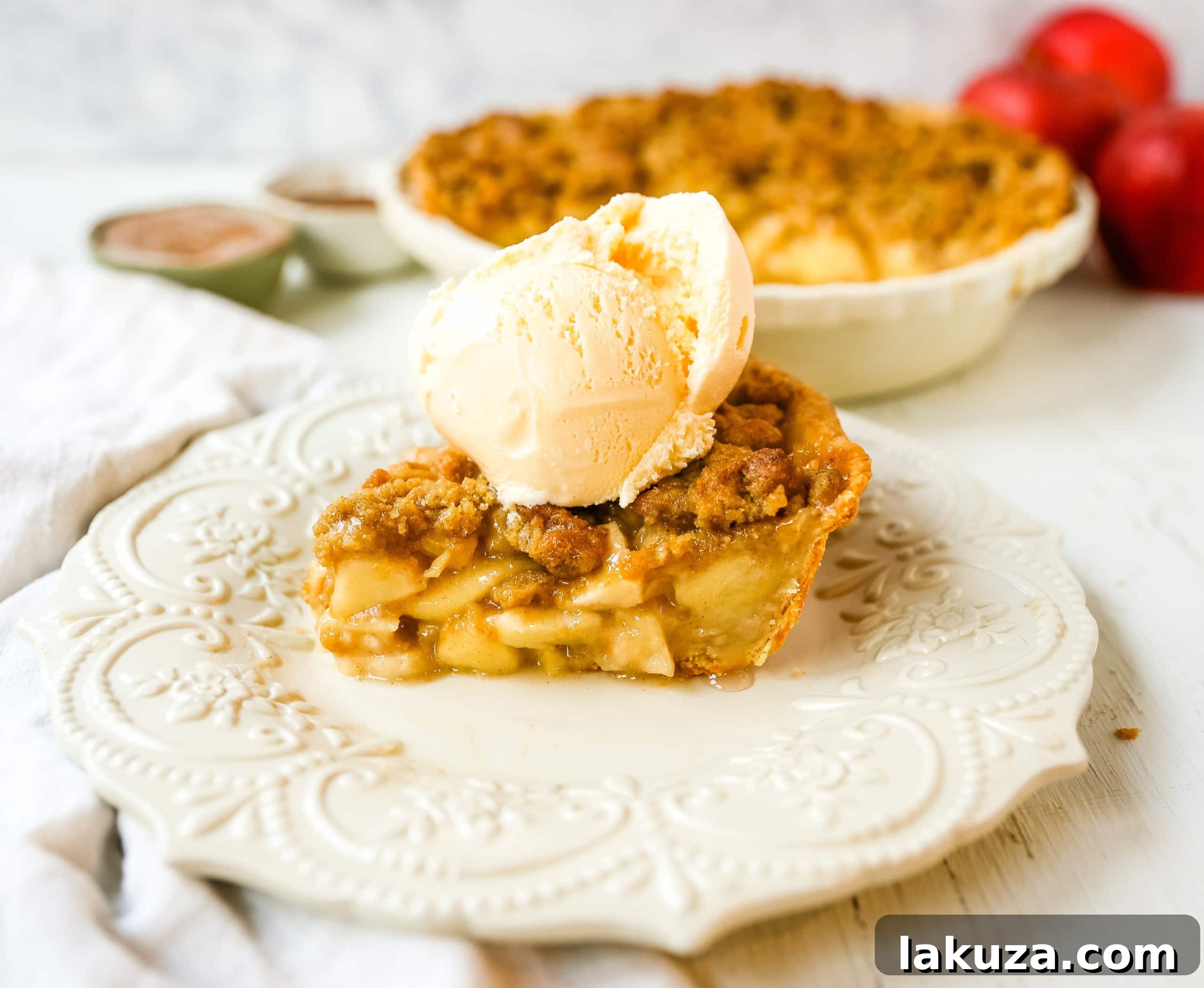 Authentic Dutch Apple Crumble 7 A beautifully presented Dutch apple pie slice on a plate with vanilla ice cream and a spoon.