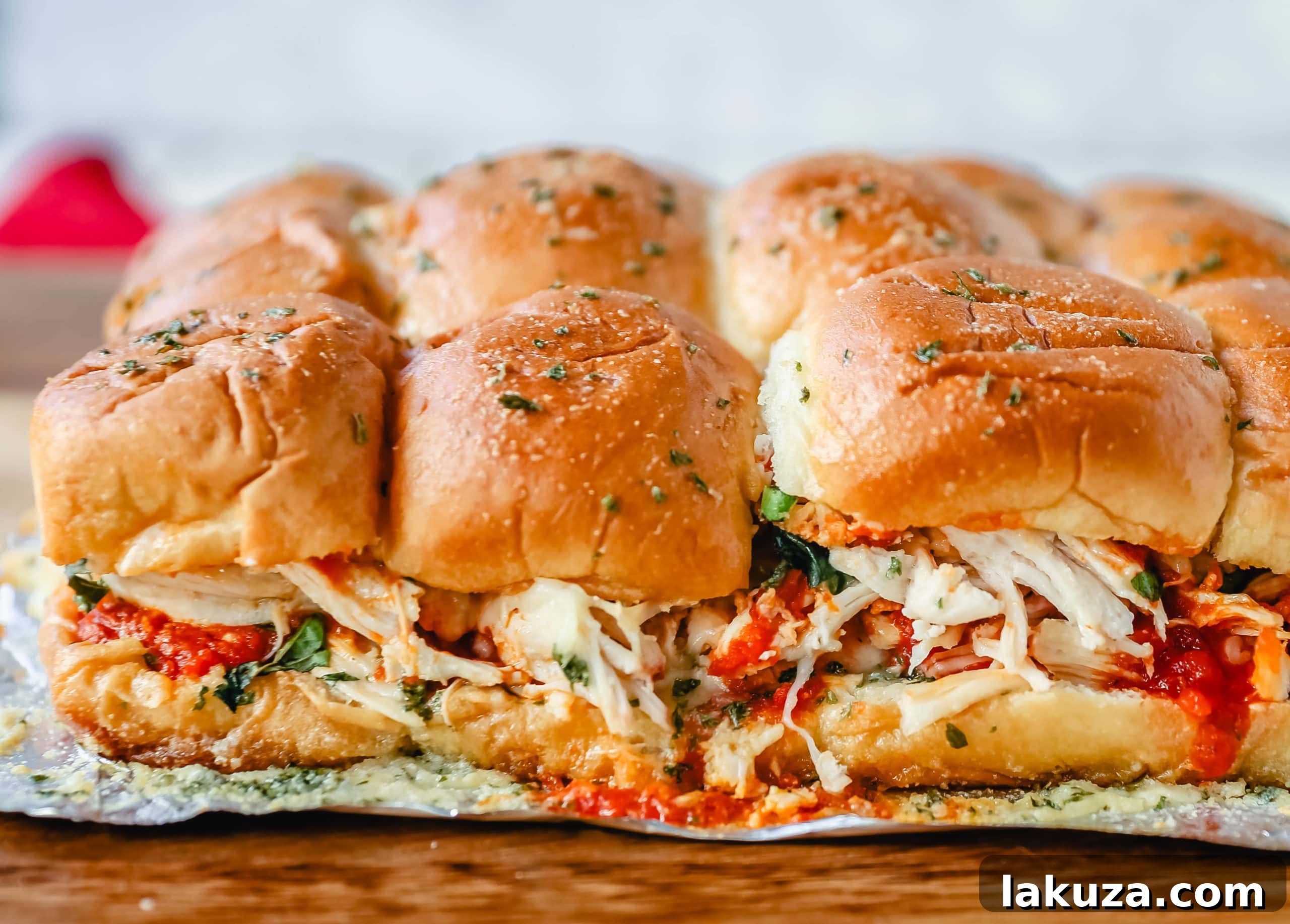 A delicious tray of uncooked Baked Chicken Parm Sliders layered with chicken, marinara, mozzarella, and basil on Hawaiian rolls, ready for the garlic butter and oven.