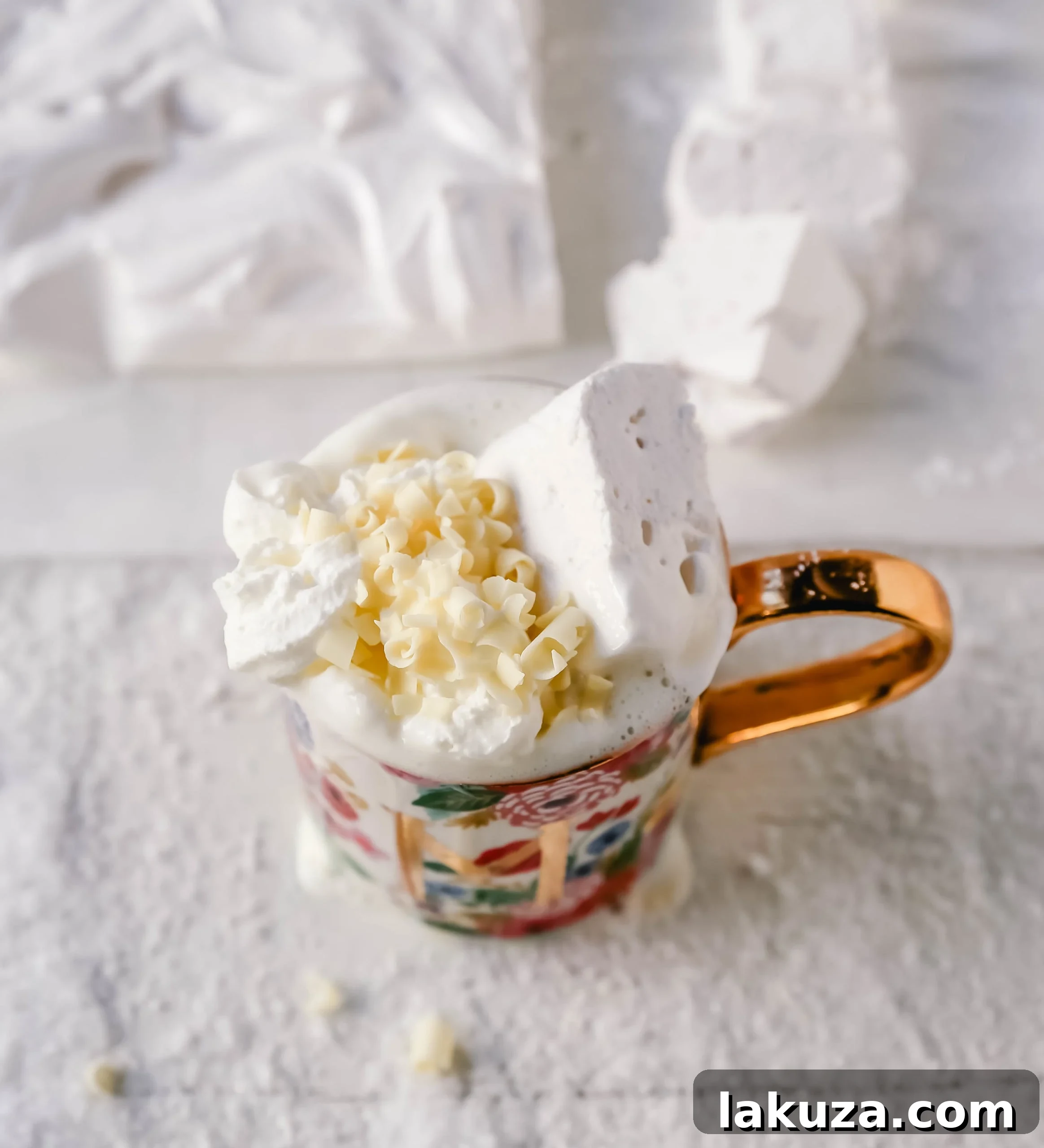 Rich and creamy homemade white hot chocolate topped with a dollop of whipped cream, homemade marshmallows, and white chocolate curls in a festive mug.