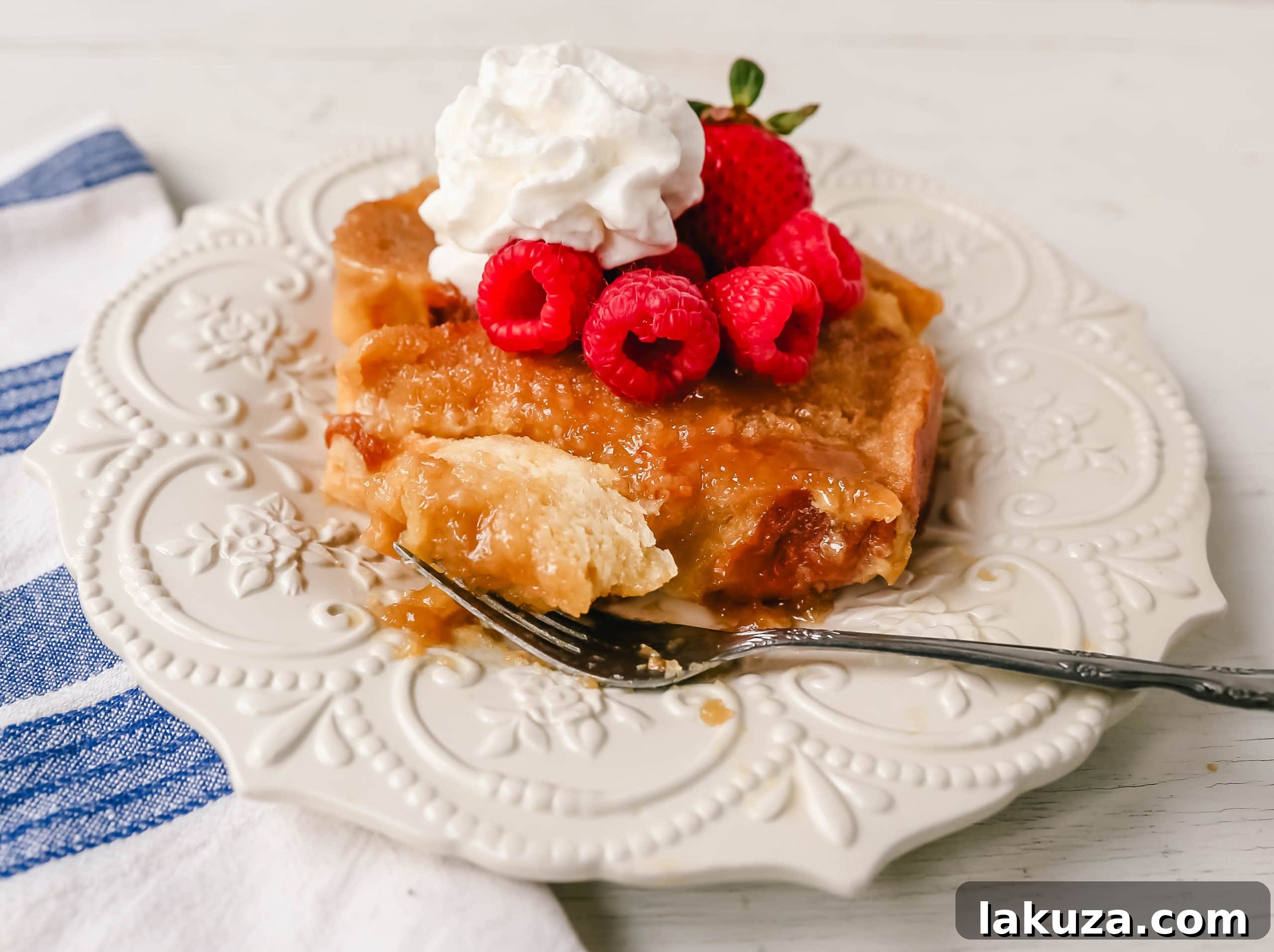 Make-Ahead Creme Brûlée French Toast Bake 4 A dish of Overnight Creme Brulee French Toast being drizzled with freshly whipped cream and topped with an assortment of colorful fresh berries, ready for serving.