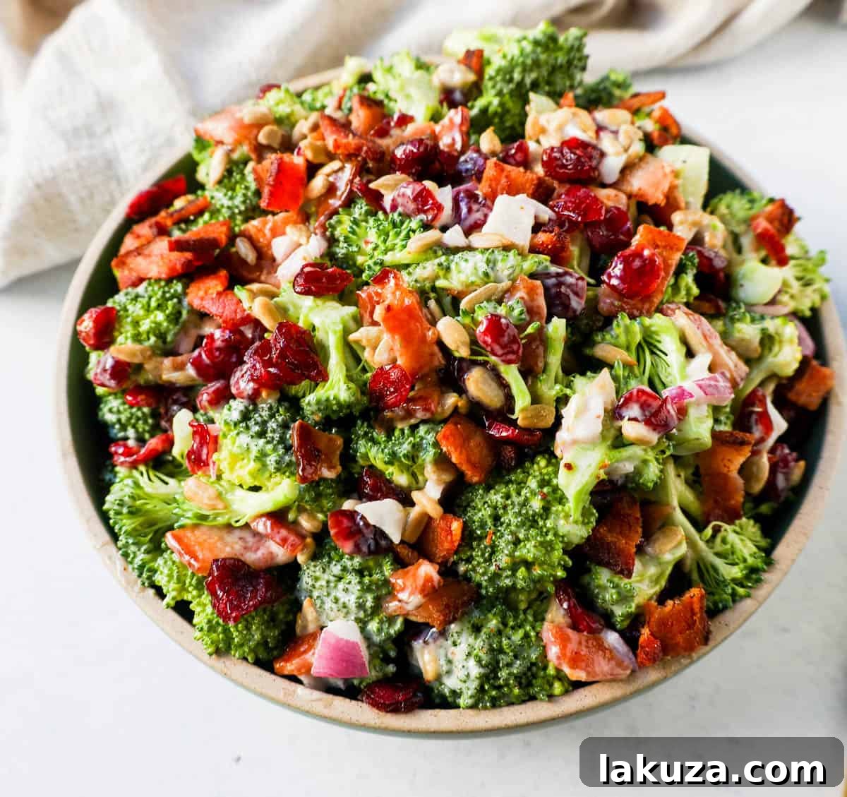A bowl of homemade broccoli salad. Crunchy, easy broccoli salad with crispy bacon, sweet dried cranberries, onion, and nuts all tossed in a sweet and tangy dressing. Tips for making the best broccoli salad. A classic potluck, BBQ, or summer side dish recipe!