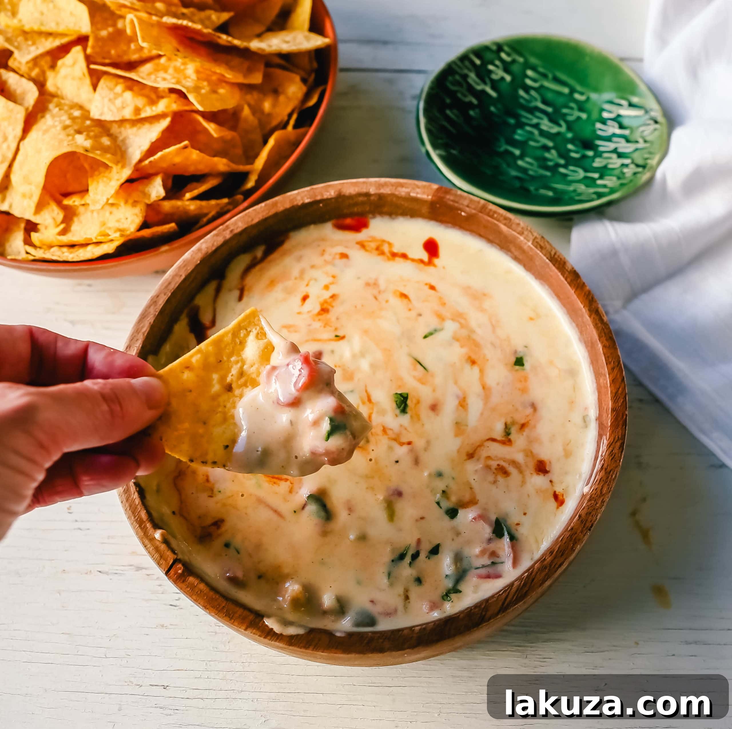 The perfect homemade green chile queso dip, garnished with fresh cilantro, a drizzle of hot sauce, and Cotija cheese. Ideal for dipping tortilla chips, topping tacos, or adding a festive touch to any meal. #queso #mexicanfoodlover #cincodemayo #appetizerrecipe
