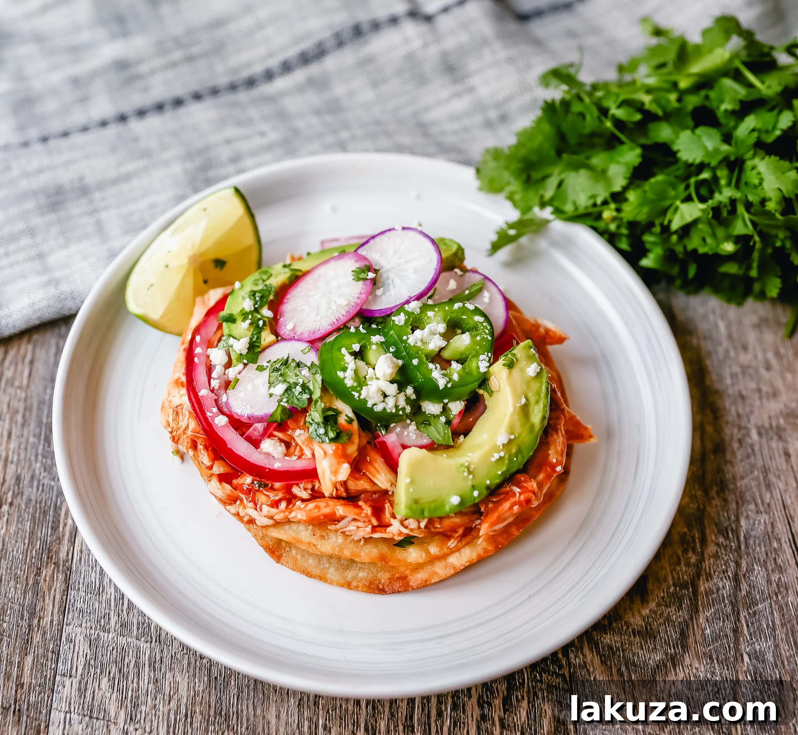 Fiesta Chicken Tostadas 3 Close-up of crispy Chicken Tostadas with vibrant toppings: seasoned chicken, melted cheese, fresh avocado, red onion, and cilantro