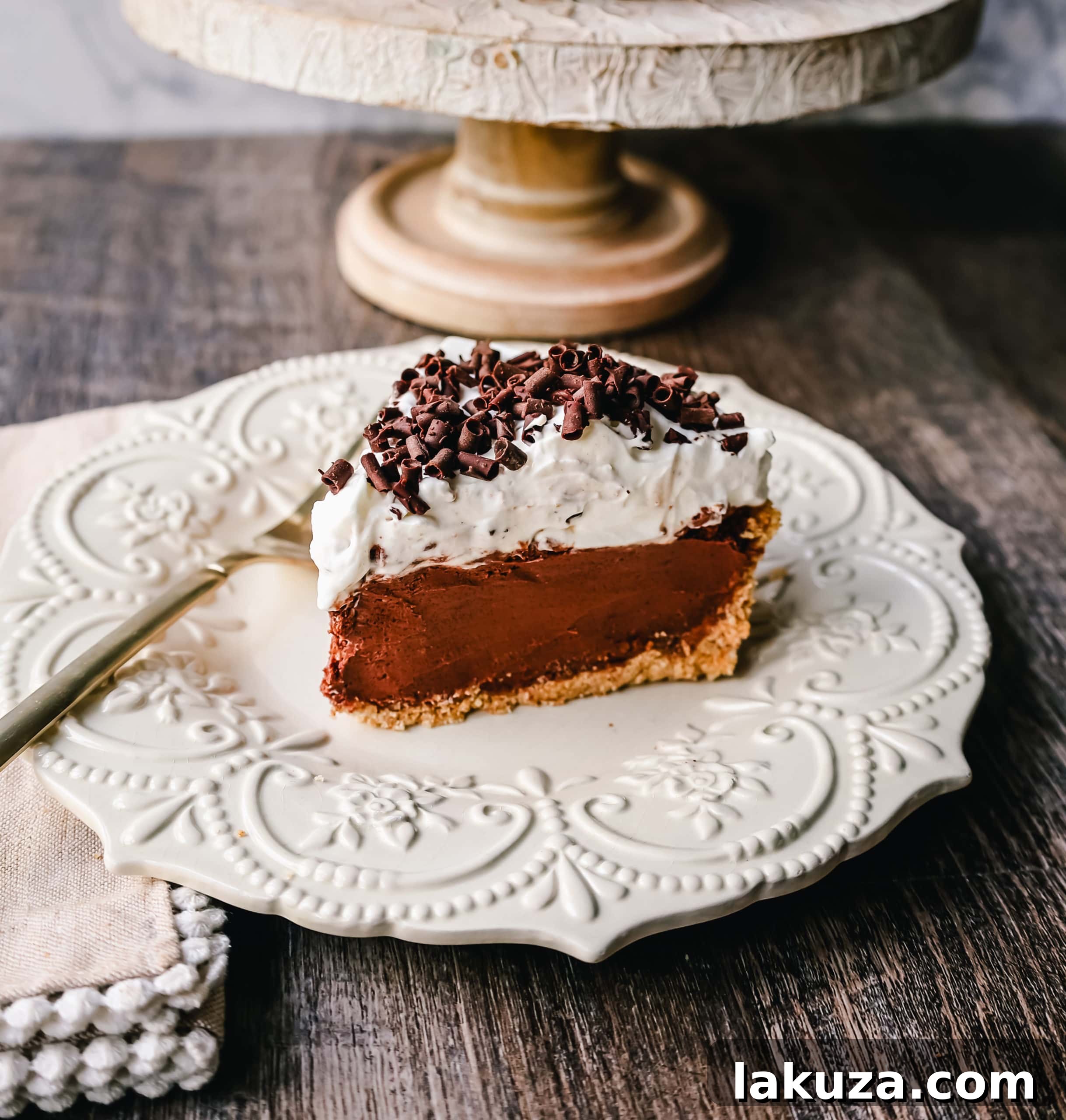 A stunning slice of French Silk Pie, showcasing layers of silky chocolate filling, fluffy whipped cream, and chocolate curls, ready to be enjoyed.