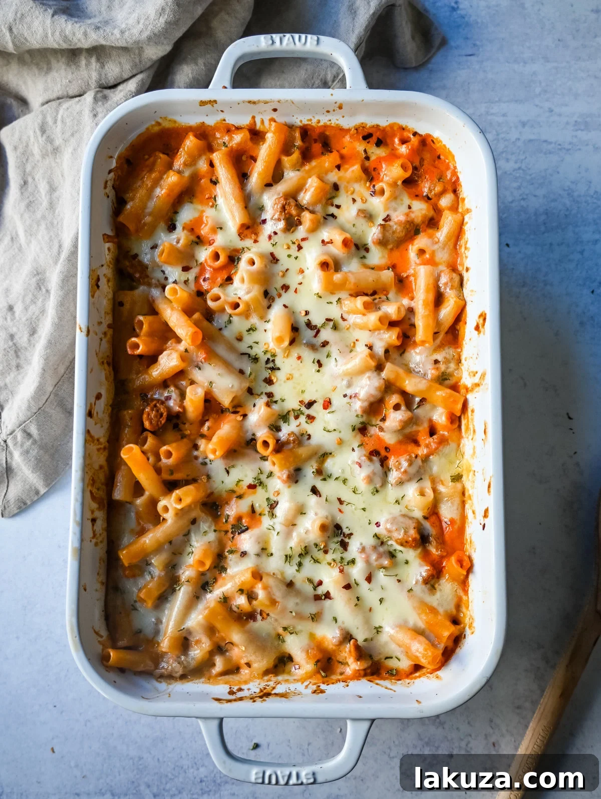 Ingredients for Baked Ziti laid out on a kitchen counter: pasta, sausage, tomatoes, cheese, herbs.