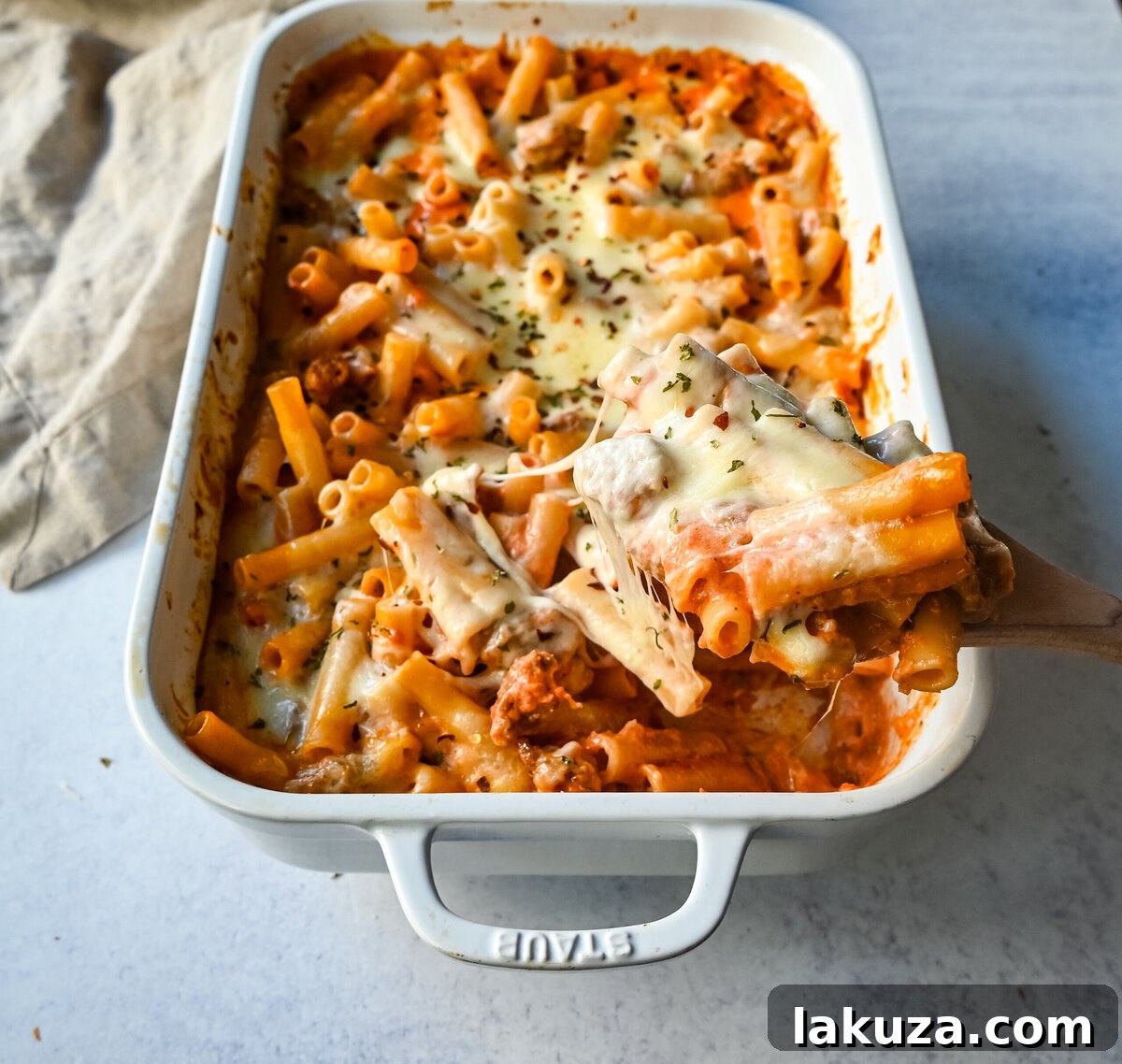 Close-up of baked ziti in a baking dish, fresh out of the oven, with steam rising.