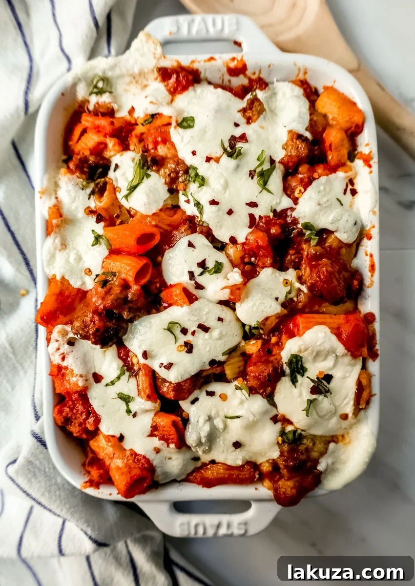 A slice of cheesy baked ziti being lifted from the dish with a serving spoon.