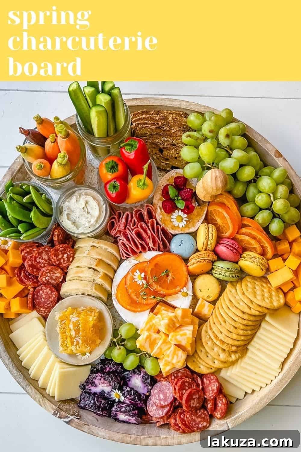 Fresh Spring Grazing Board 5 A wide shot of an elegant Spring Charcuterie Board, richly laden with a variety of cheeses, sliced fruits, cured meats, crackers, and sweet macarons, all artfully arranged for a festive occasion.