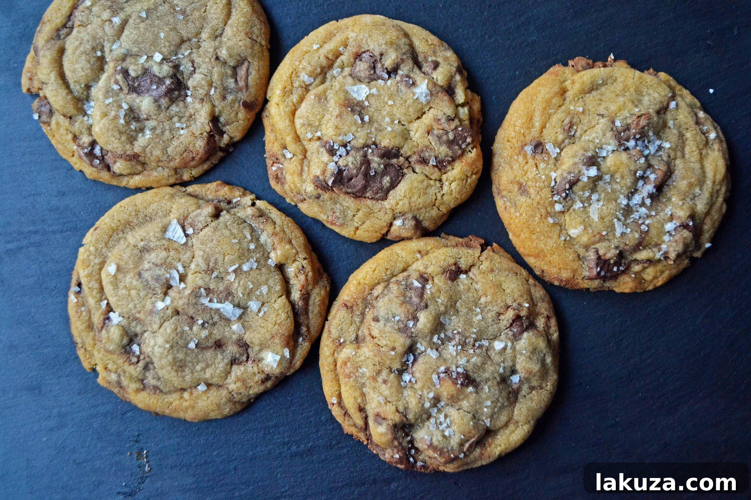 A close-up of a perfectly round, thick browned butter chocolate chip cookie, featuring generously sized chocolate chunks.