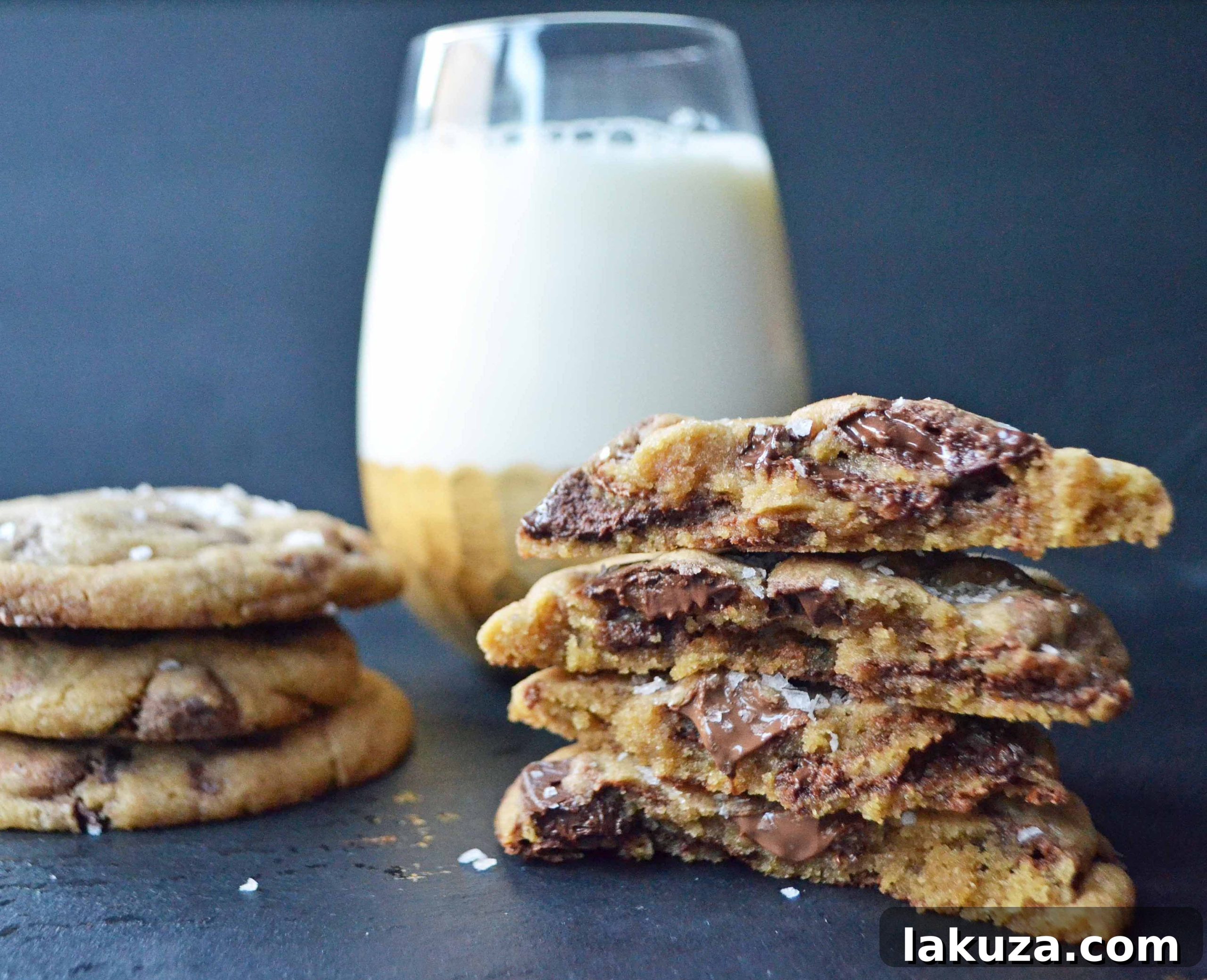 A hand reaching for a warm browned butter chocolate chip cookie, with a delicate dusting of sea salt on top.