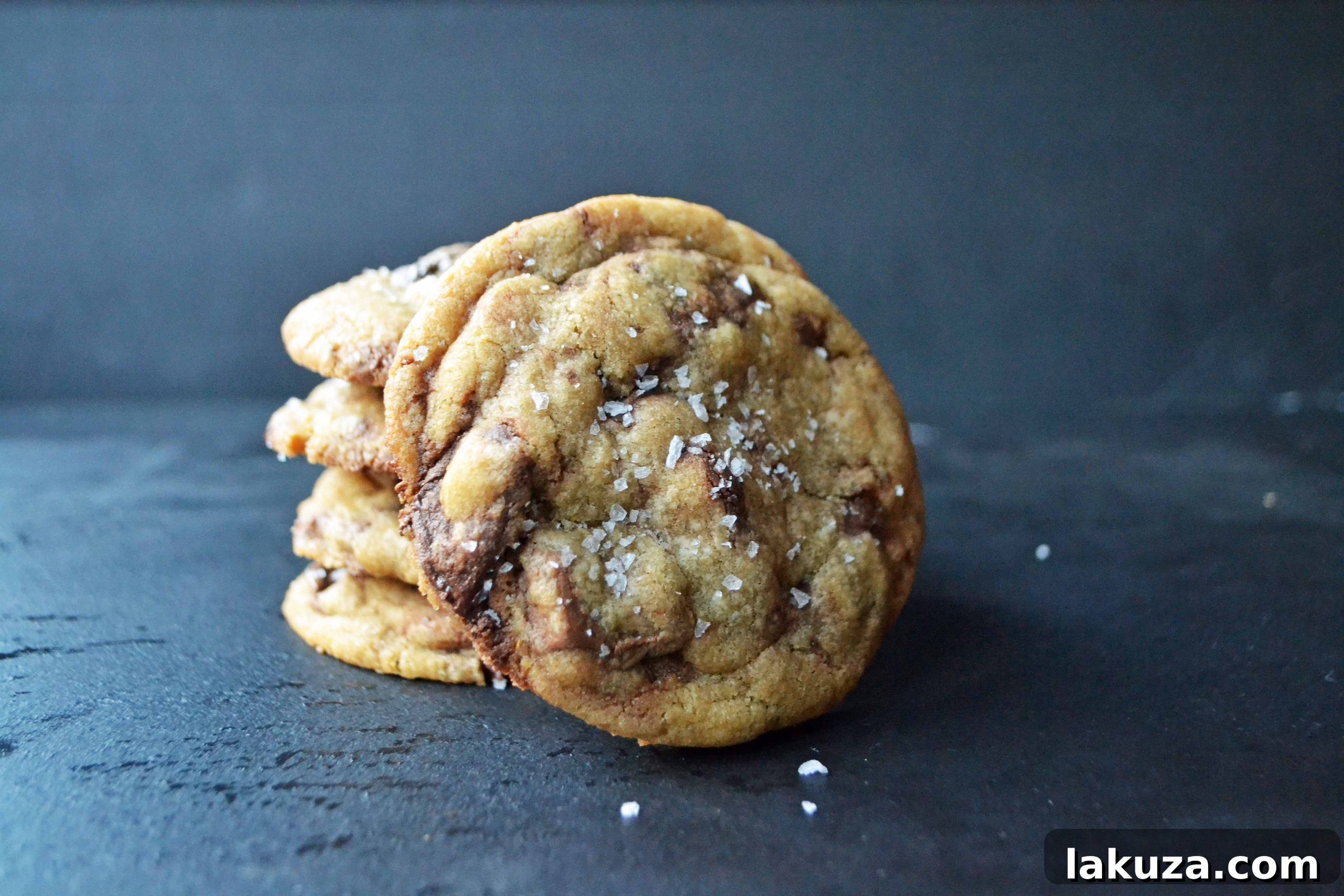 A beautifully presented stack of freshly baked browned butter chocolate chip cookies on a rustic wooden board.