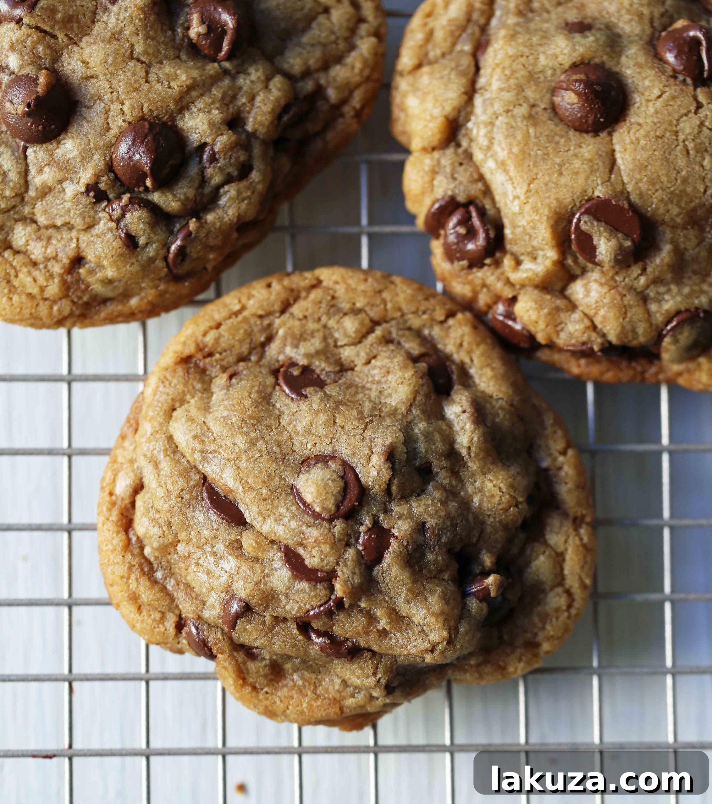 A close-up view of golden-browned butter chocolate chip cookies, each adorned with a generous sprinkle of sea salt flakes.