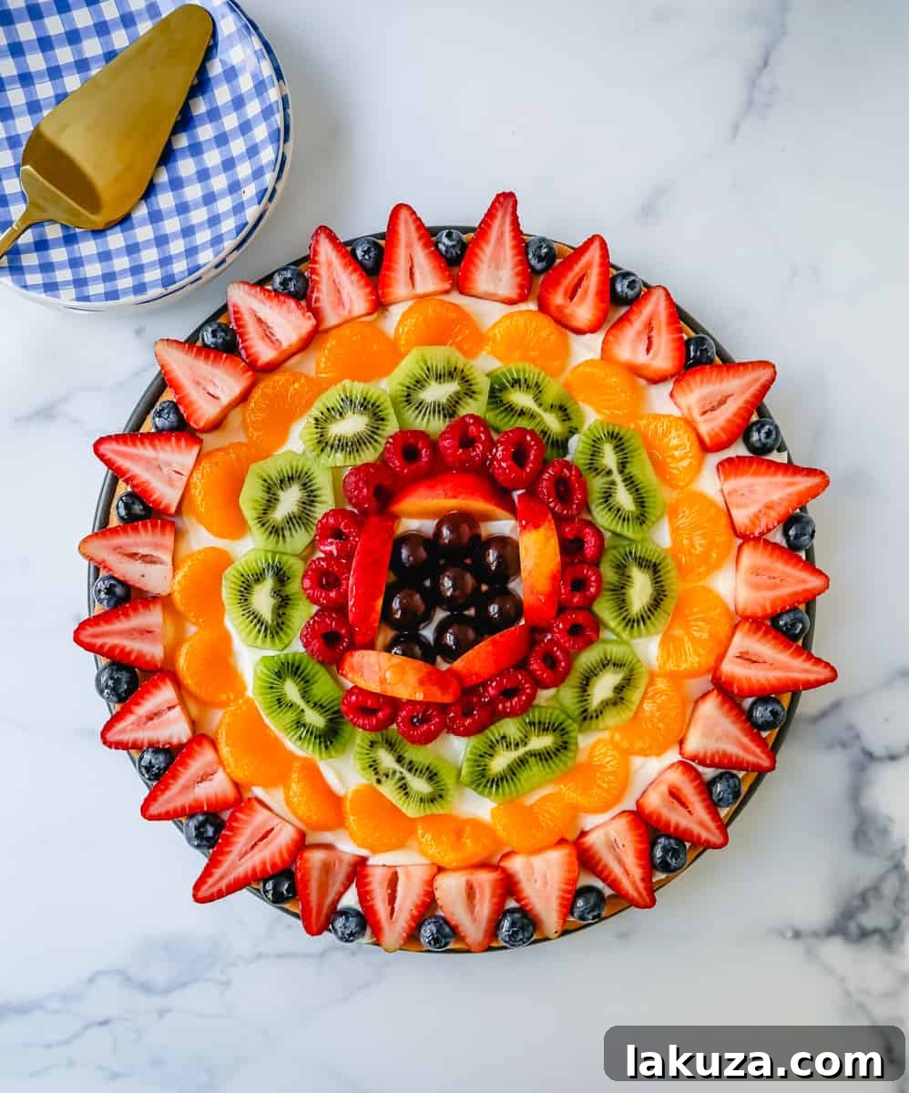 Sugar Cookie Fruit Tart 3 A close-up of a slice of fruit pizza with sugar cookie crust, showcasing the layers of cookie, frosting, and colorful fruit.