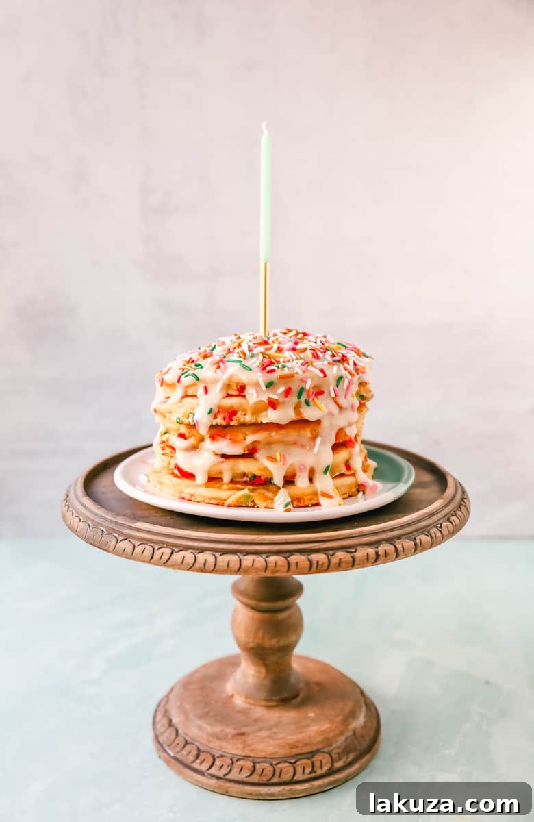 Close-up of golden-brown buttermilk funfetti pancakes, studded with vibrant rainbow sprinkles, stacked high and topped with a luscious cream cheese glaze.