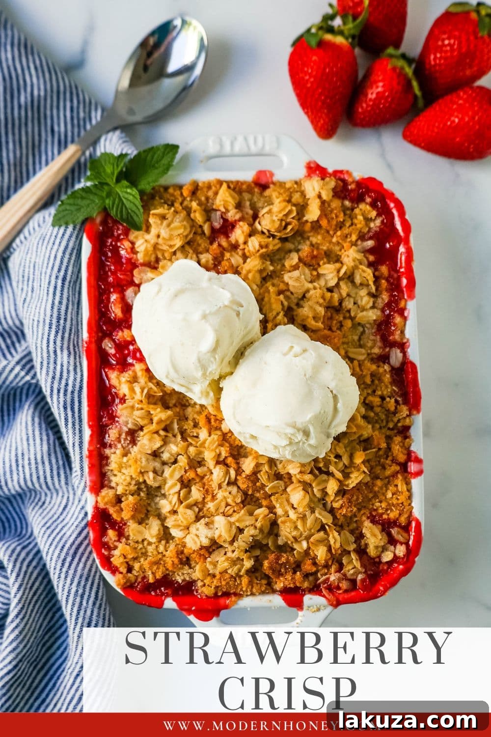 A large serving of Strawberry Crisp in a white baking dish, showing the bountiful golden-brown oat crumble on top of the red, bubbly strawberries.